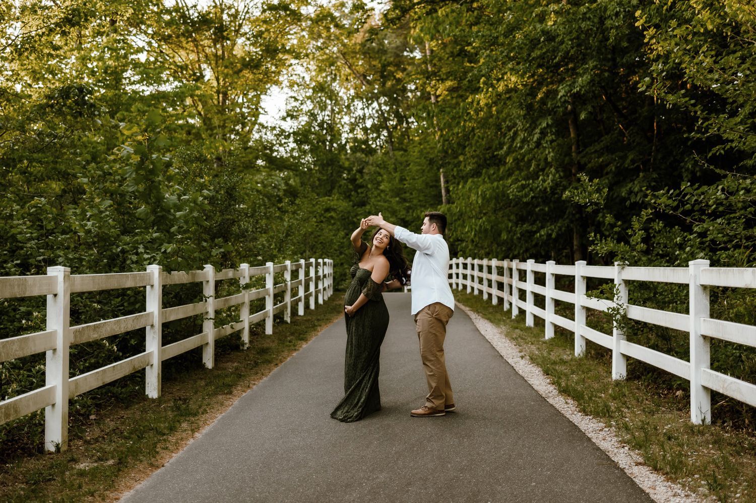 Expectant couple twirling together on a paved trail during a Raleigh maternity photography session