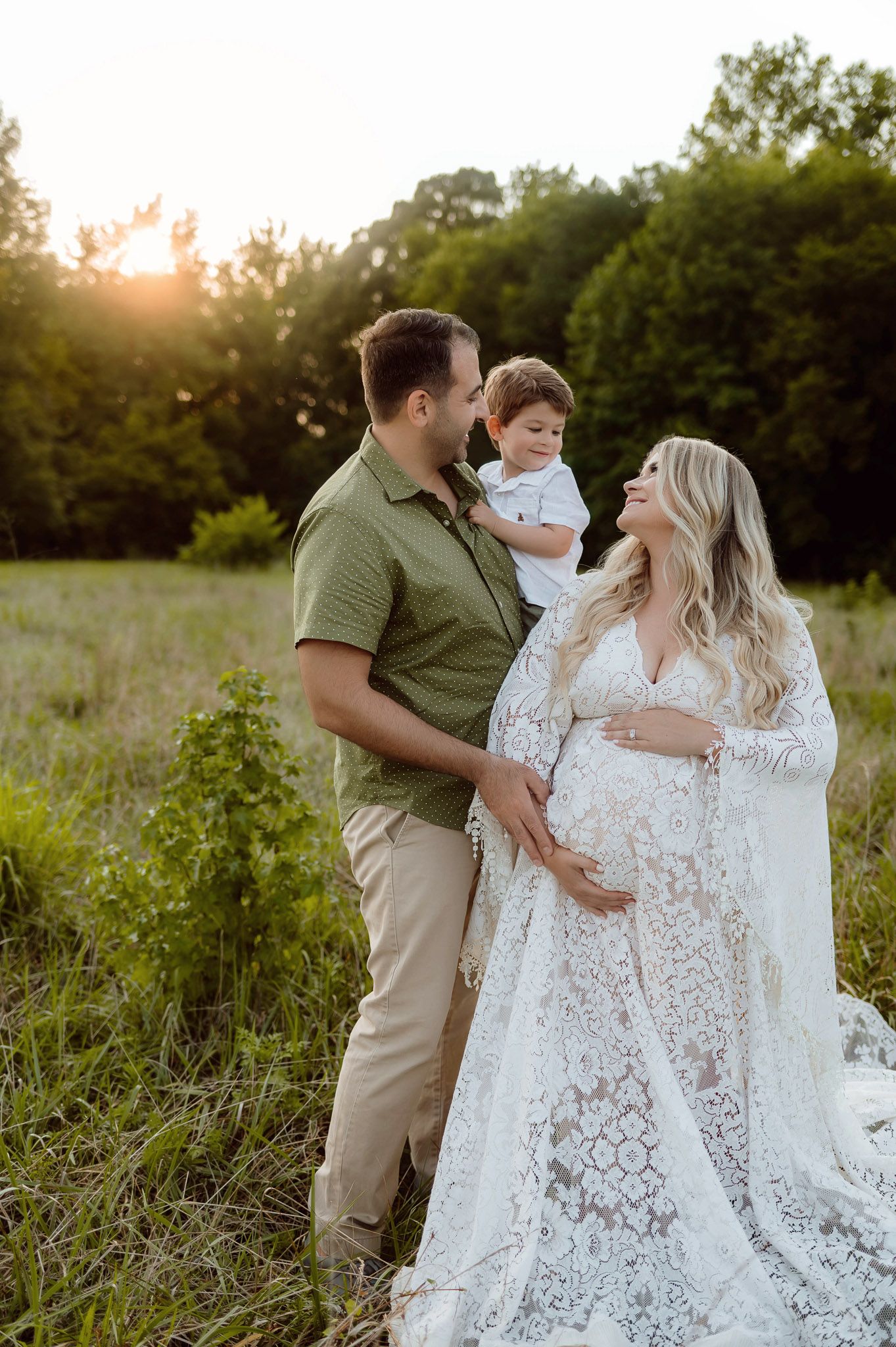 Pregnant mother standing beside her husband holding their toddler during an outdoor maternity photo session in Raleigh North Carolina