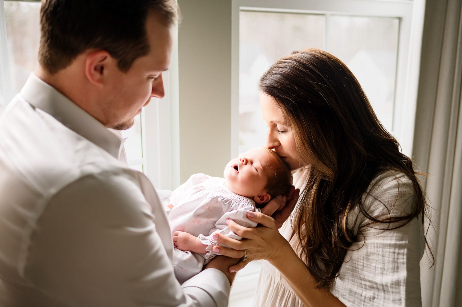 Parents holding their newborn baby near a window during a natural light in-home newborn photography session in Raleigh NC