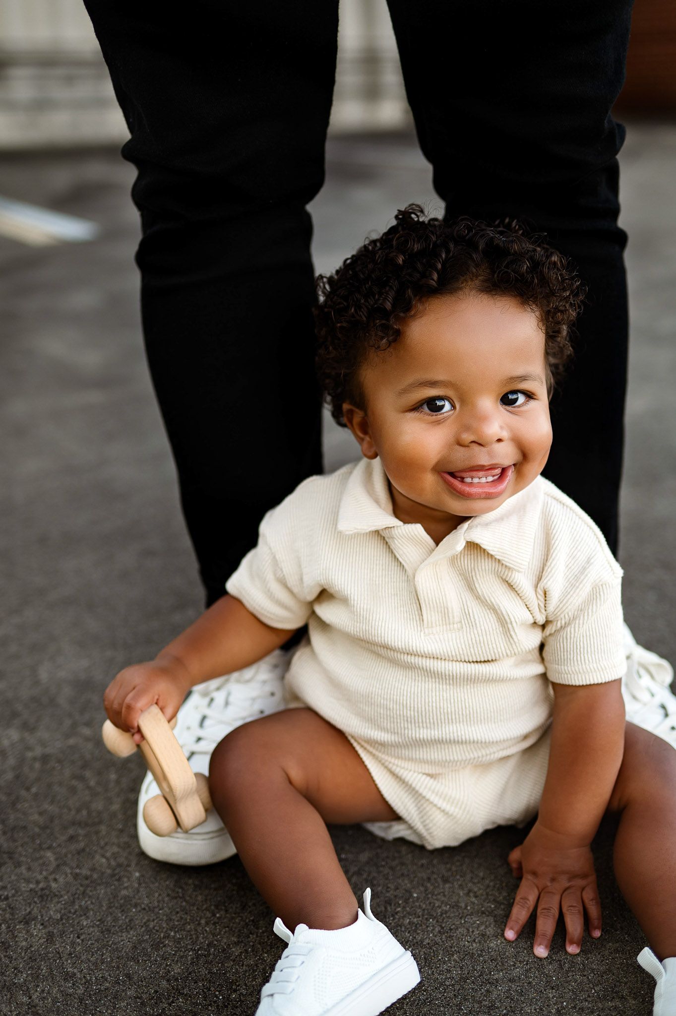 Smiling toddler sitting on the ground holding a wooden toy during a downtown Raleigh family photography session