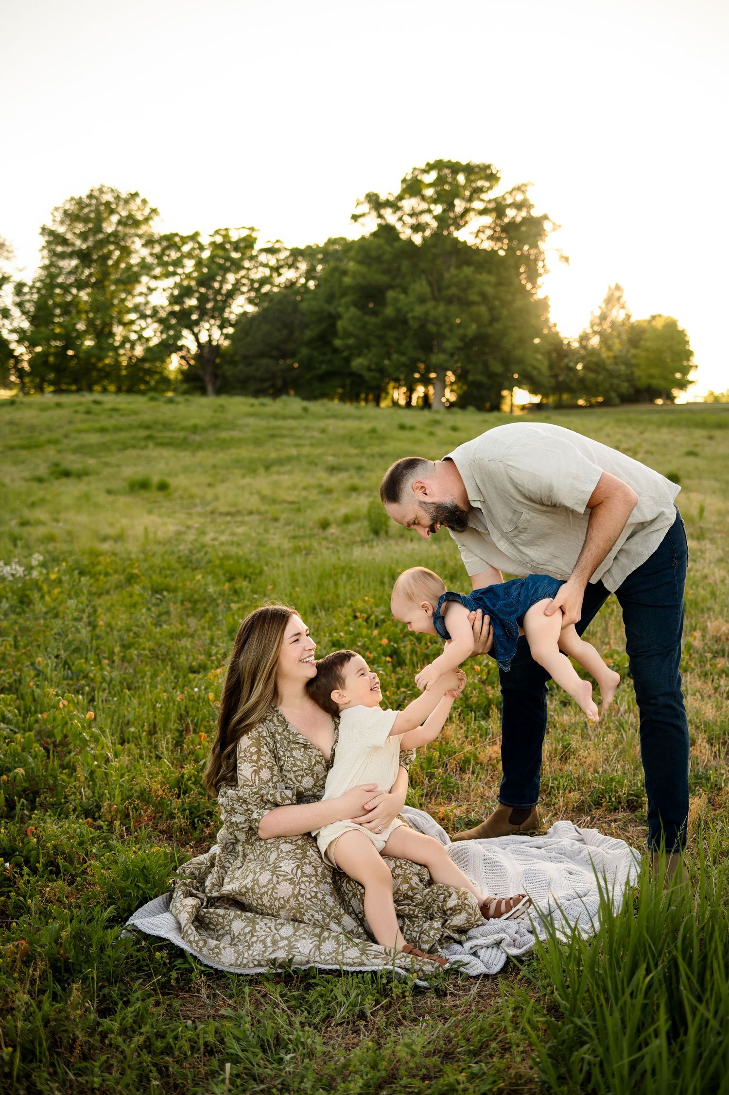 Playful family moment with dad lifting baby while mom and toddler laugh during sunset with a Raleigh family photographer