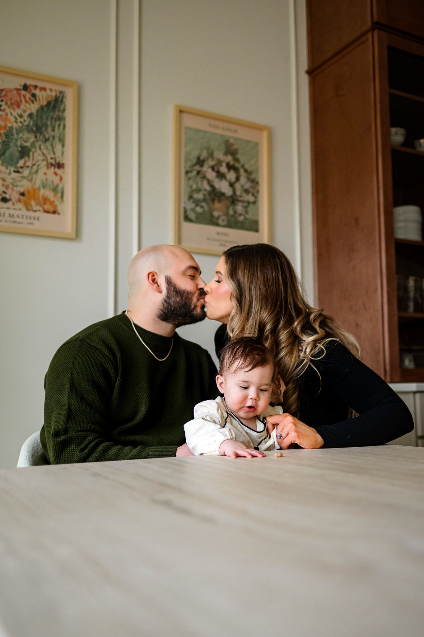 Parents sharing a kiss while their baby plays on the table during a candid in-home family photography session
