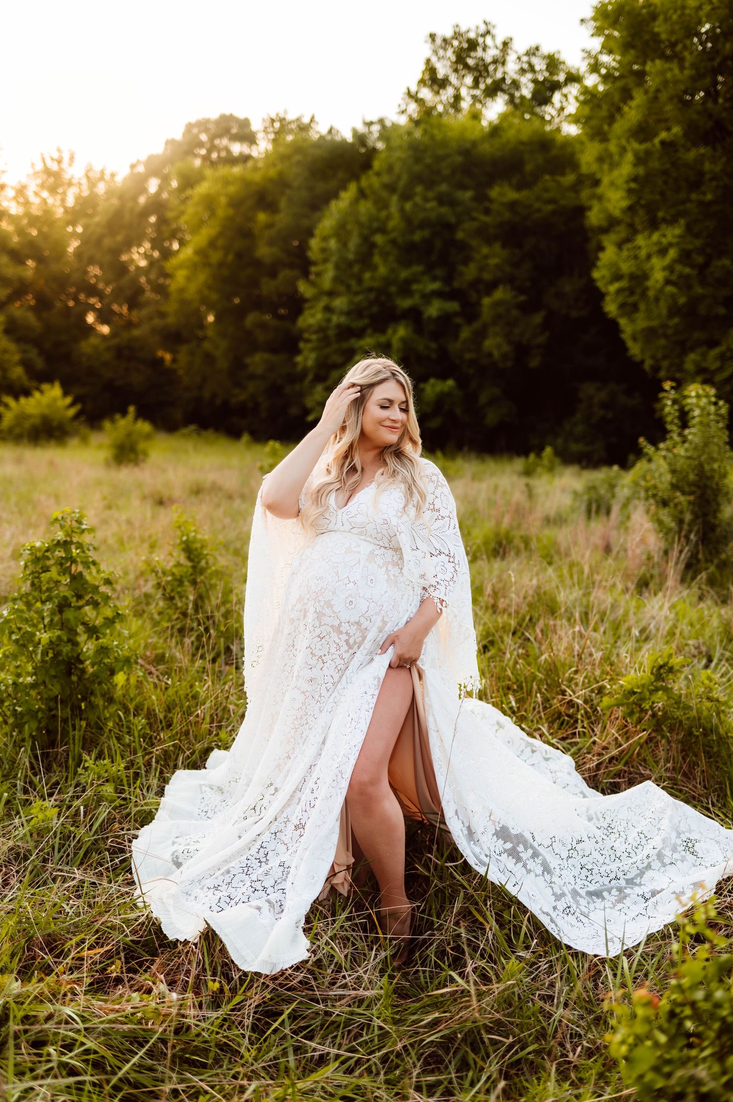 A tender moment at sunset in a meadow as a mother in a flowing white lace dress is photographed by best maternity photographer raleigh