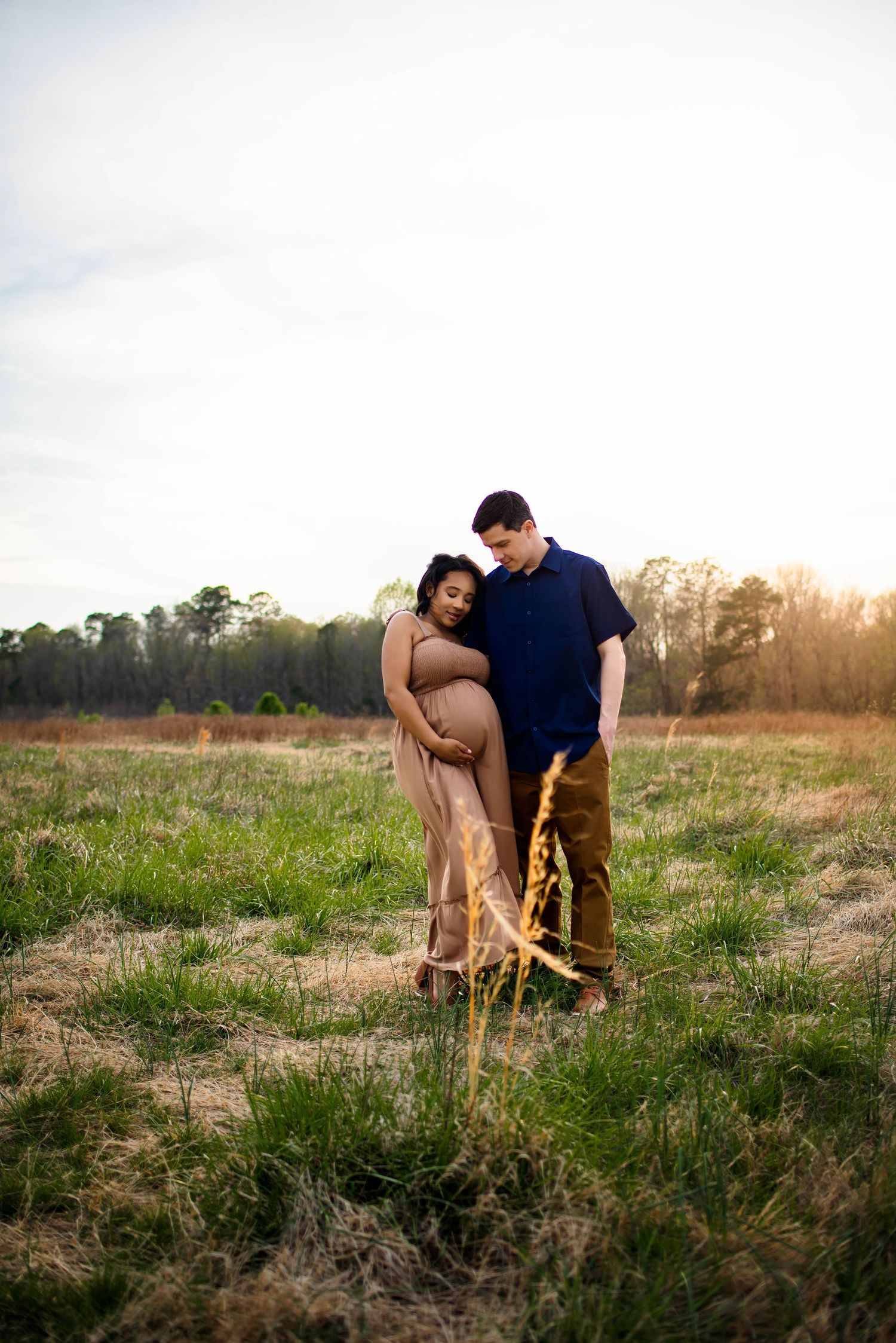 A couple standing together in a grassy field at sunset, sharing an intimate maternity moment with raleigh maternity photographer