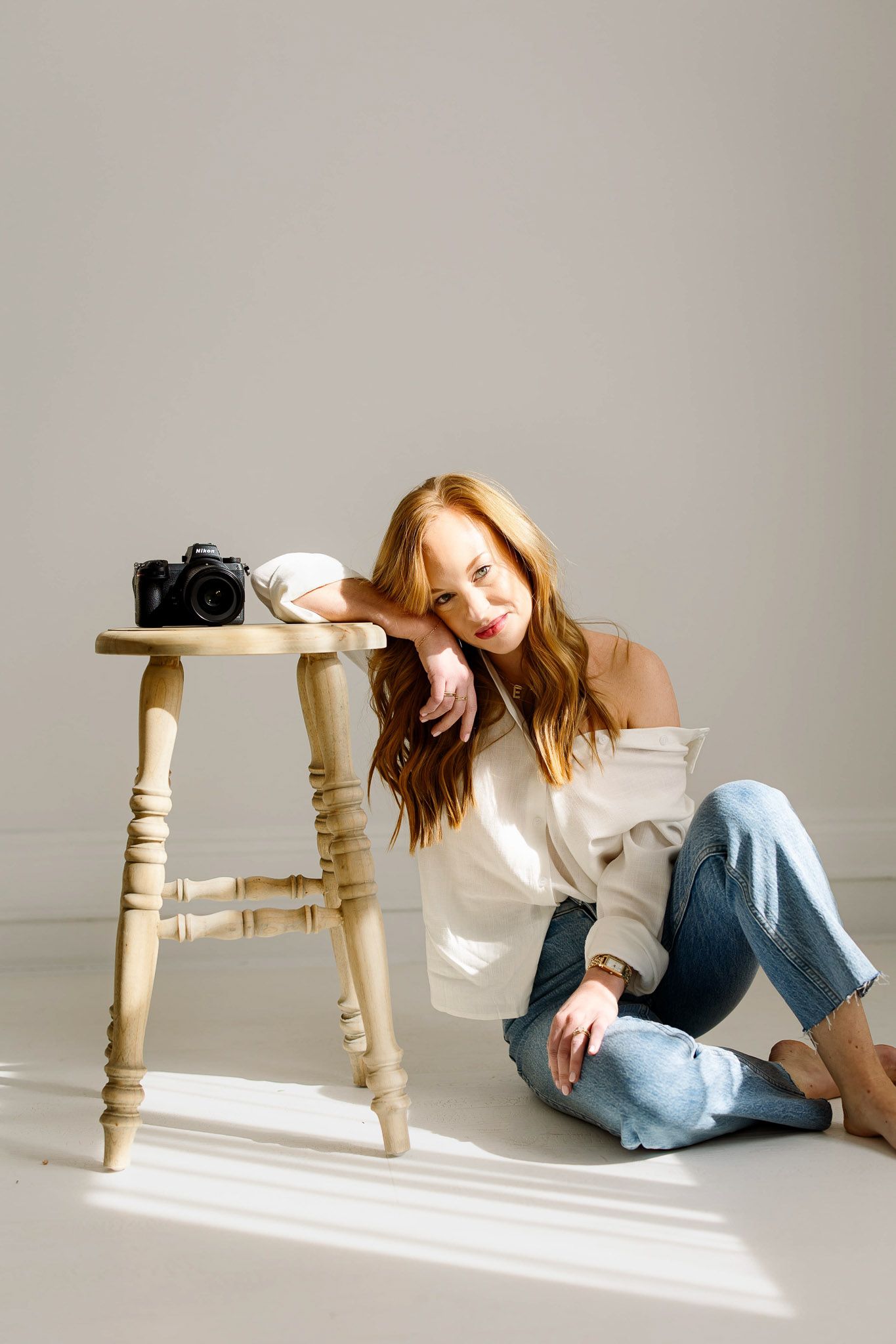 Emma Branch Raleigh family photographer sitting beside stool with camera in a natural light studio portrait