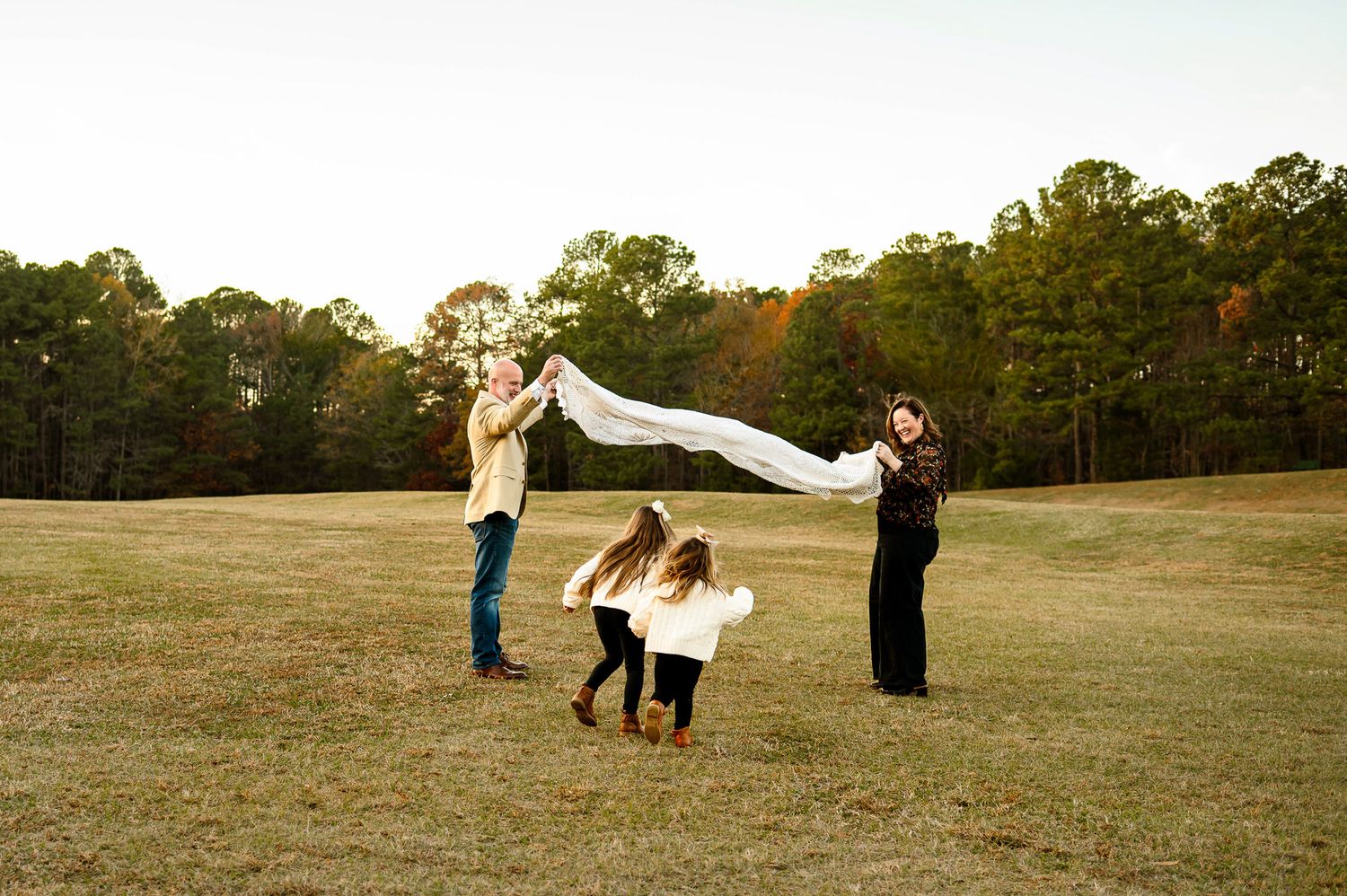 Parents lifting blanket as children run underneath during playful outdoor family photography session near Raleigh NC