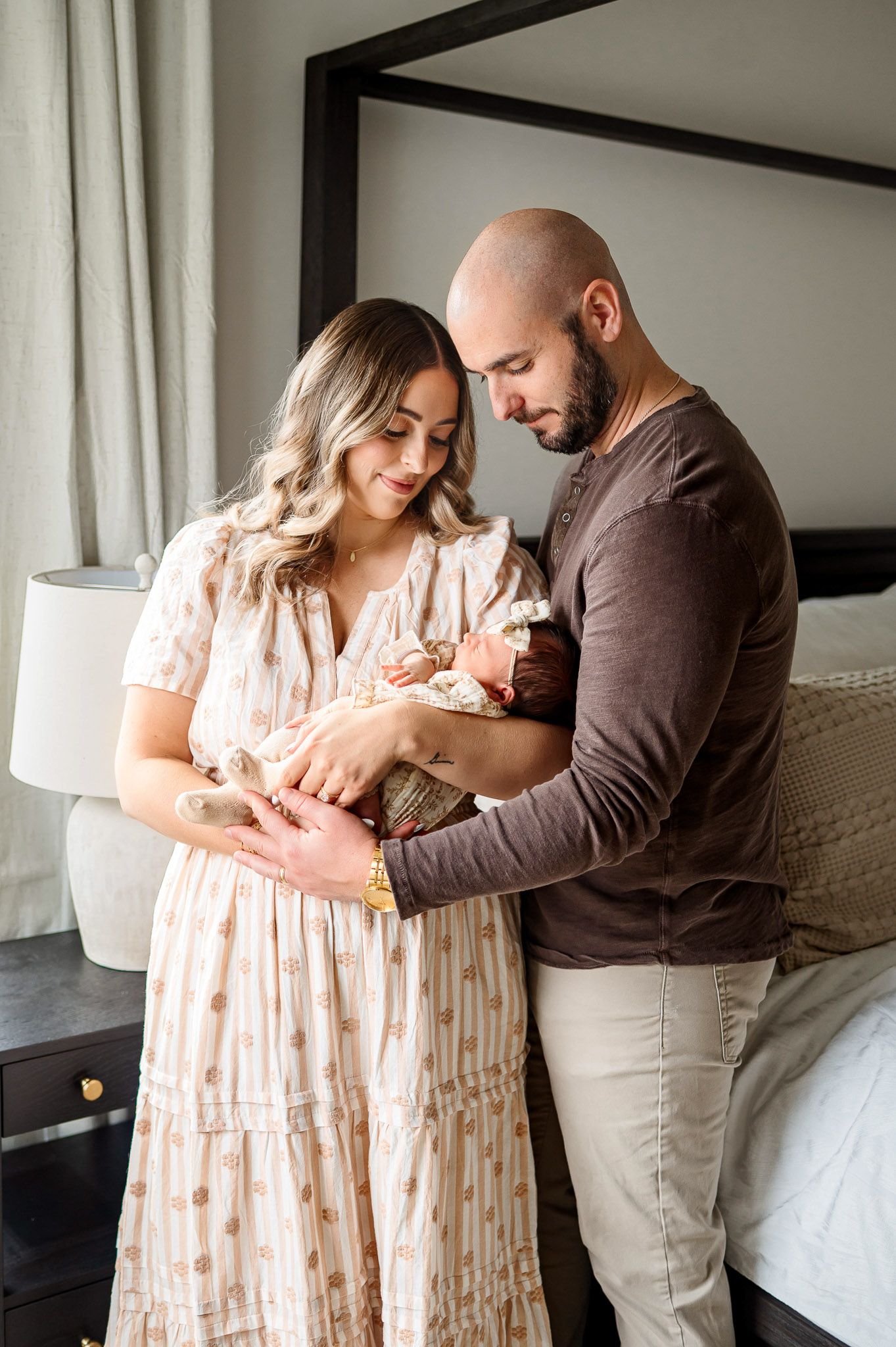 Parents standing together holding their newborn baby in a bright bedroom during a lifestyle newborn photography session in the Triangle area