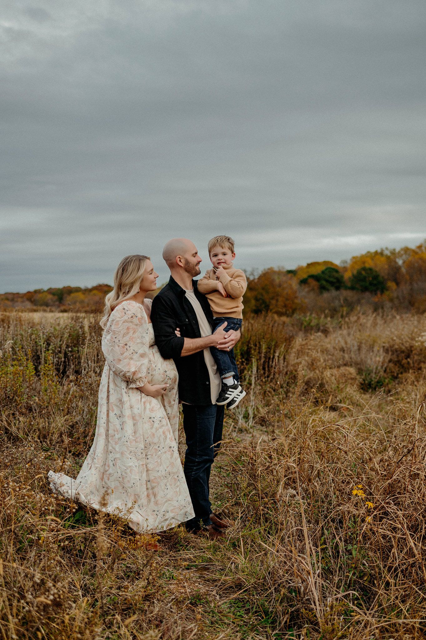 Family maternity photography portrait with parents and toddler standing together in an open field near Raleigh NC