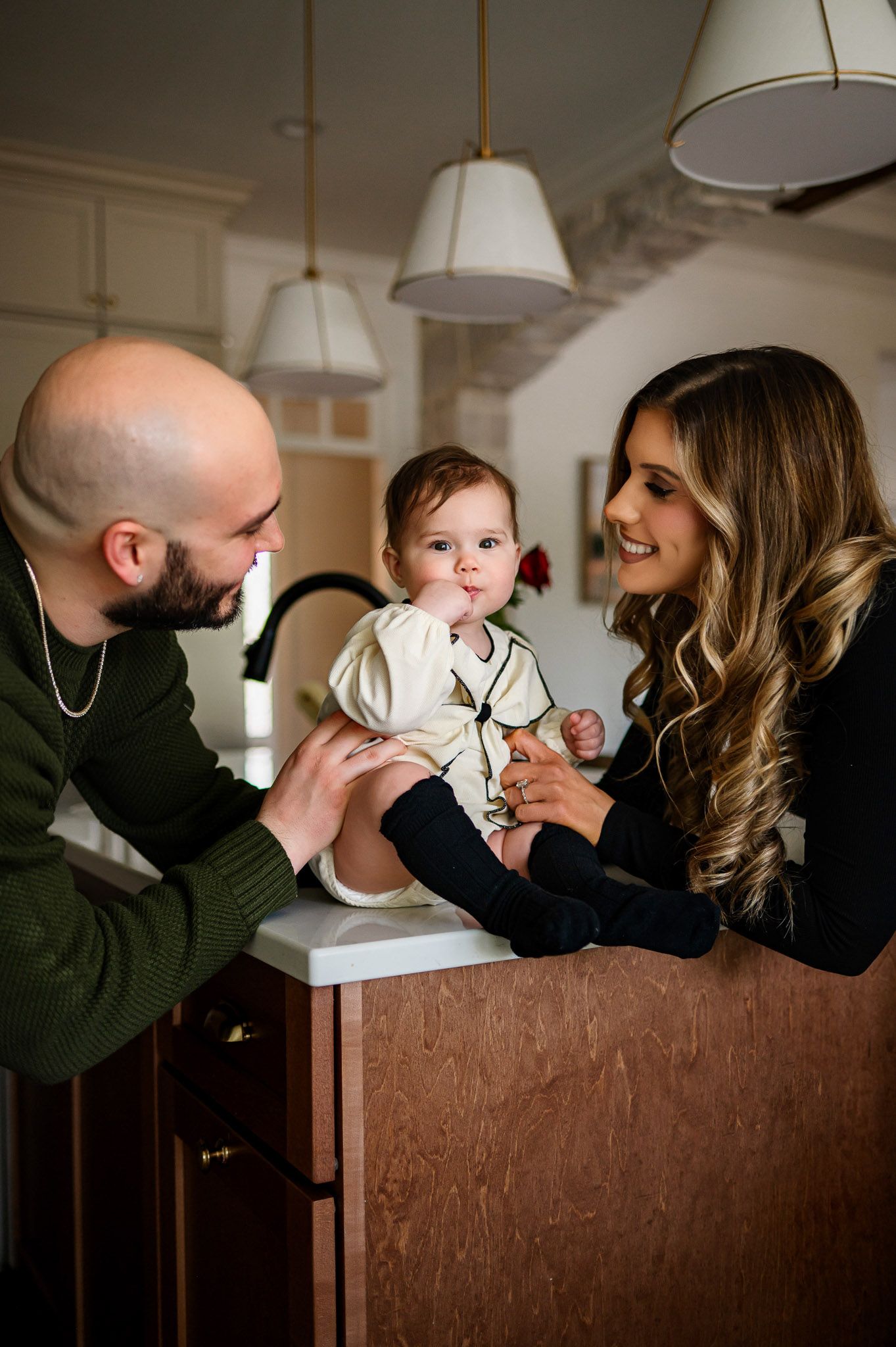 Parents smiling at their baby sitting on the kitchen counter during an in-home family photography session in Raleigh NC