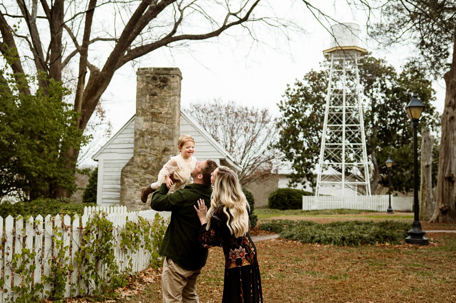 Father lifting his toddler into the air while mother stands nearby during a playful outdoor family photography session near Knightdale NC