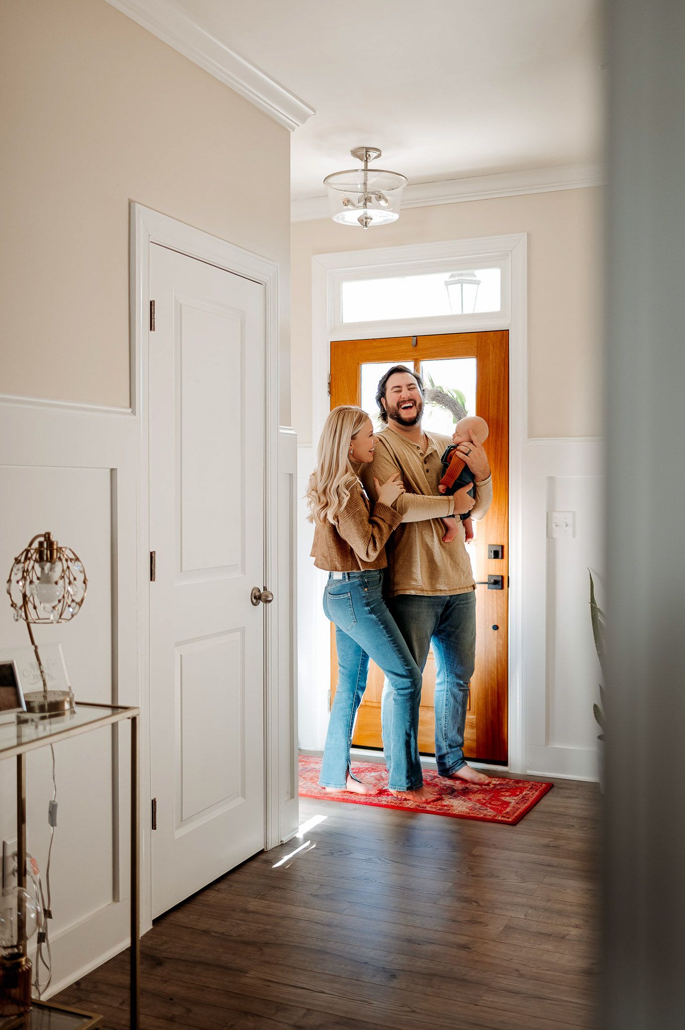 Parents standing together by their front door holding their newborn baby during an in-home newborn photography session in Raleigh NC