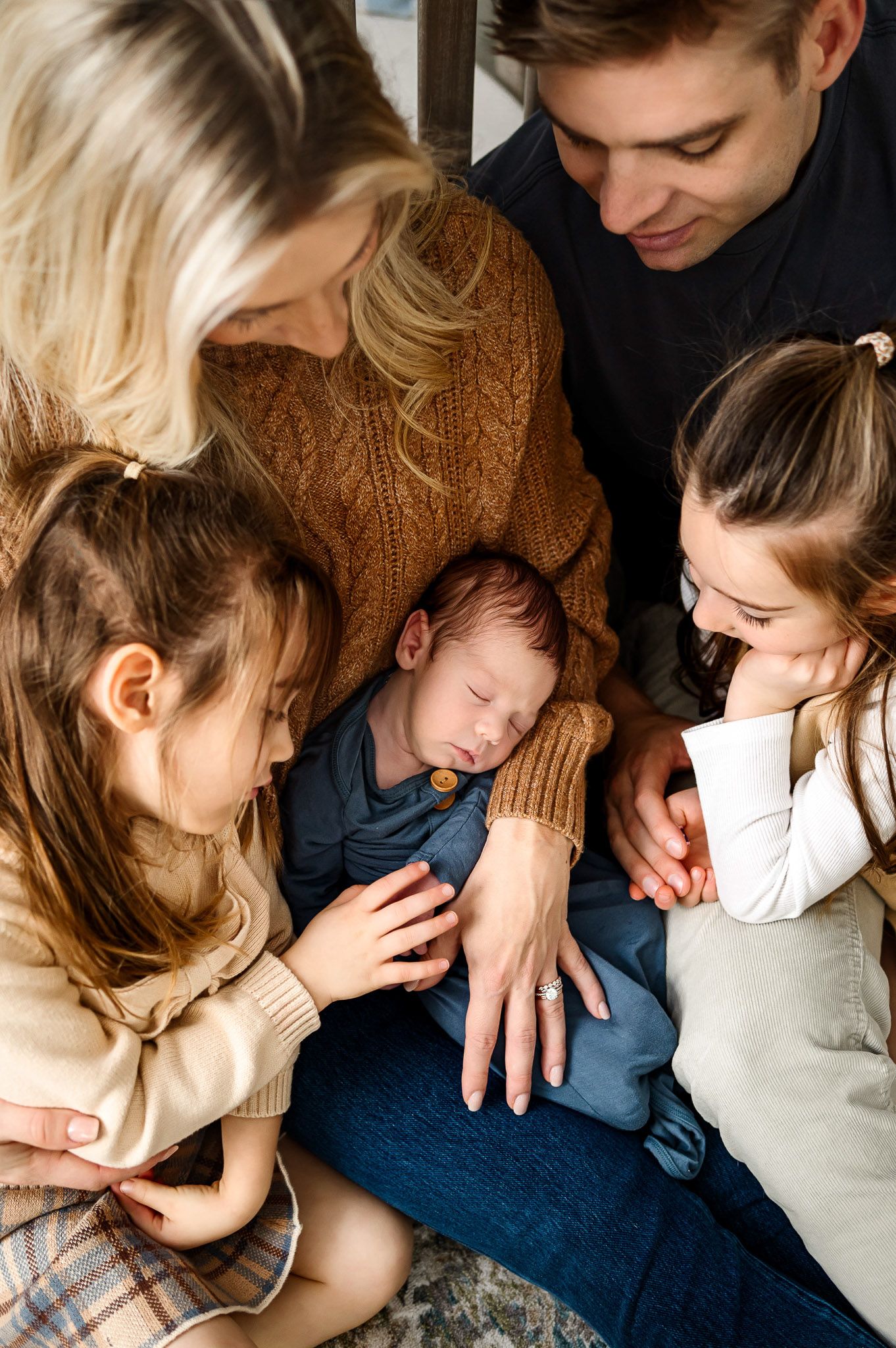Parents and siblings gathered around admiring their newborn baby during an in-home lifestyle newborn photography session