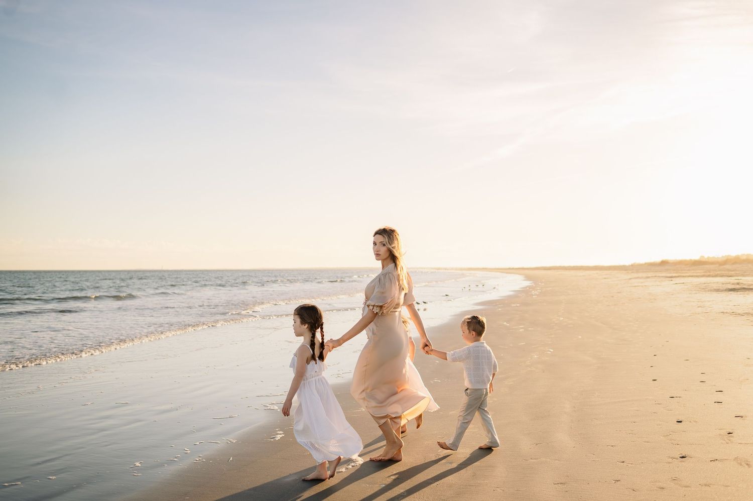 Expecting mother walks holding hands with her young children during a golden hour maternity photography session in Raleigh NC