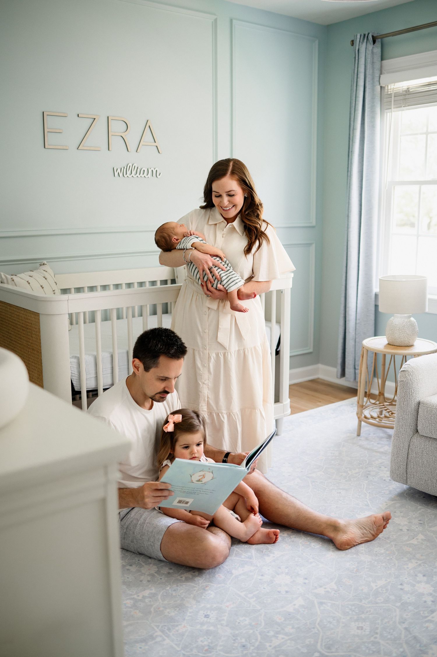 Family reading a book together in a light blue nursery during an in-home newborn photography session in Raleigh NC