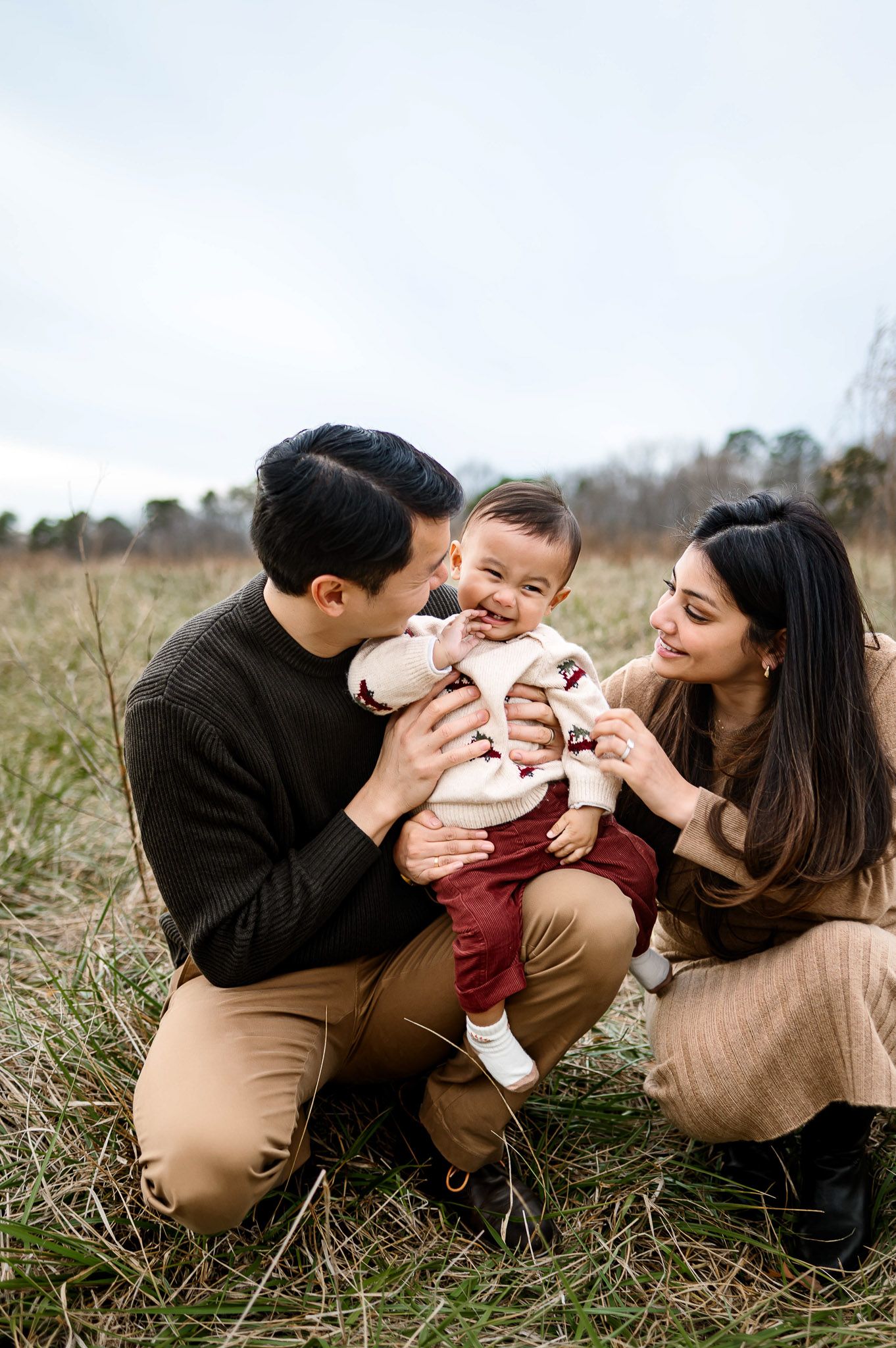 Parents kneeling in the grass while playing with their baby during an outdoor lifestyle family photography session in Apex NC