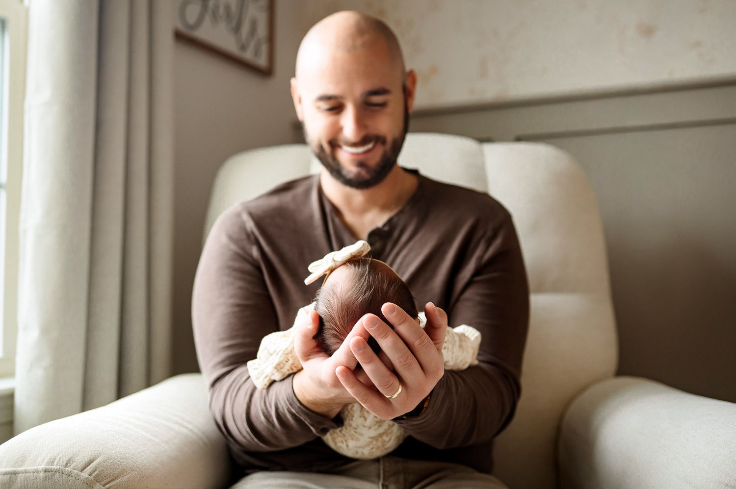 Father sitting in a chair gently holding his newborn baby during a relaxed in-home newborn photography session