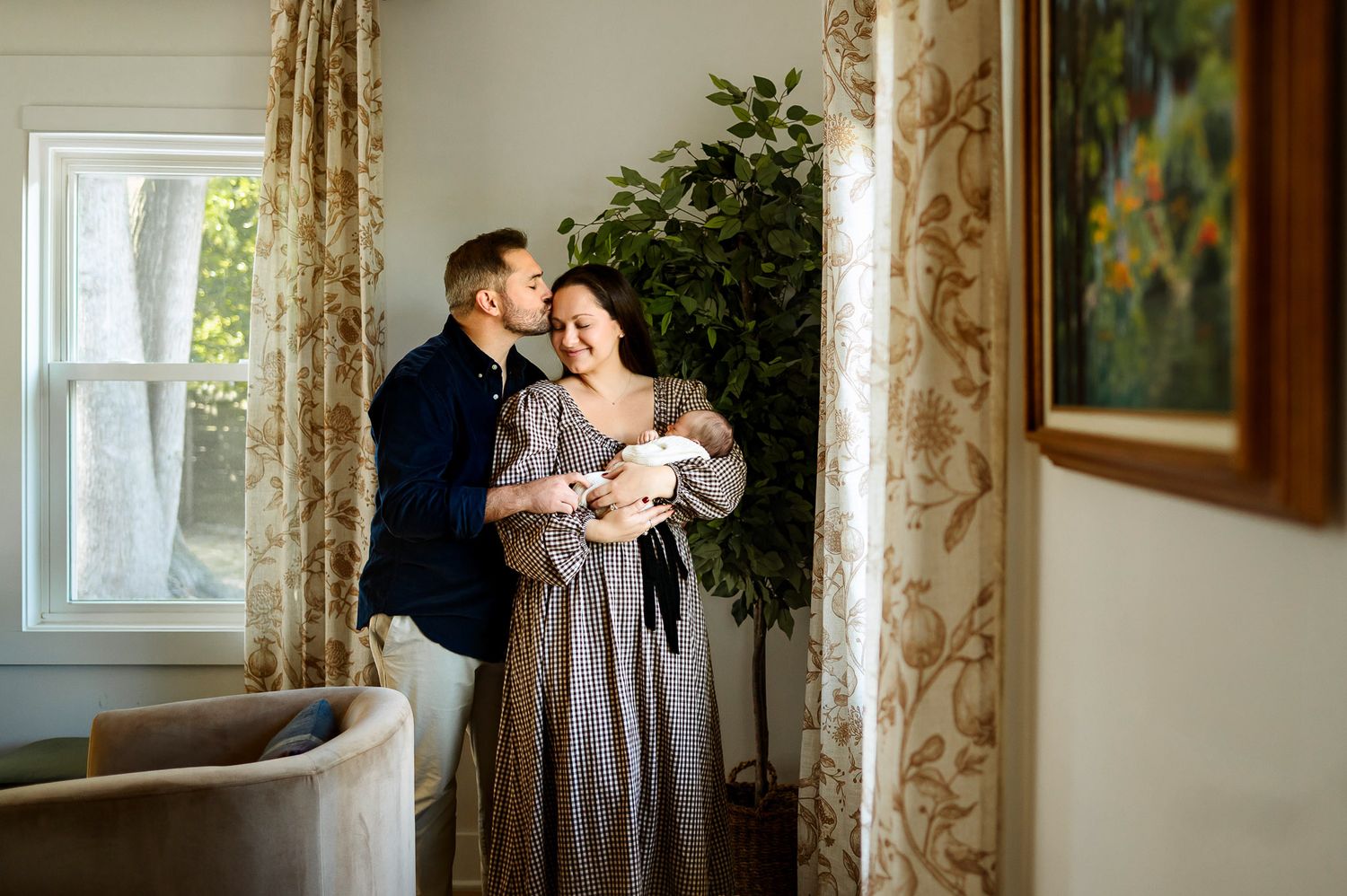 Parents standing by a window holding their newborn baby during a relaxed in-home lifestyle newborn photography session
