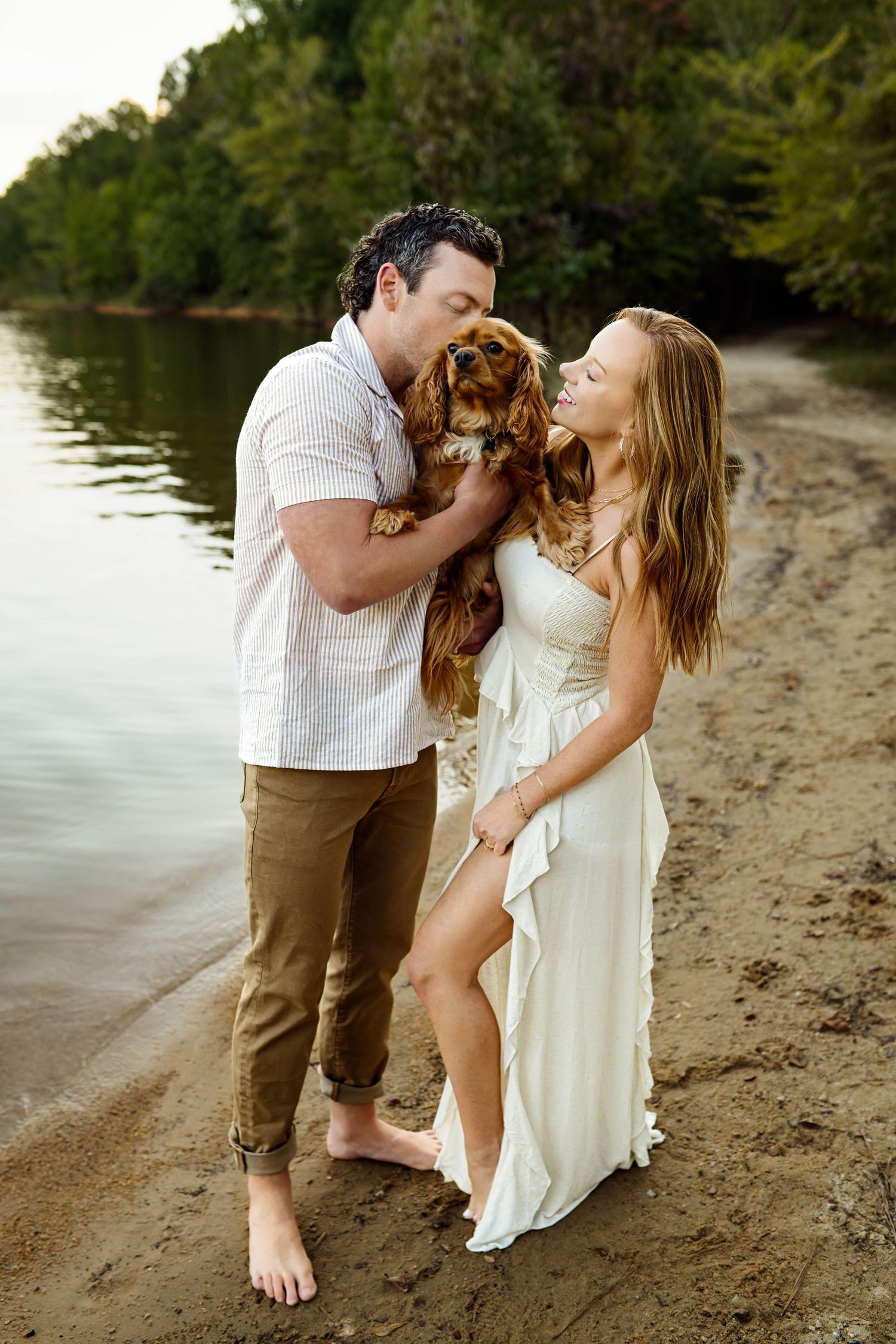 A couple shares a romantic moment on a beach with their golden retriever dog between them at sunset with Emma Branch Photography