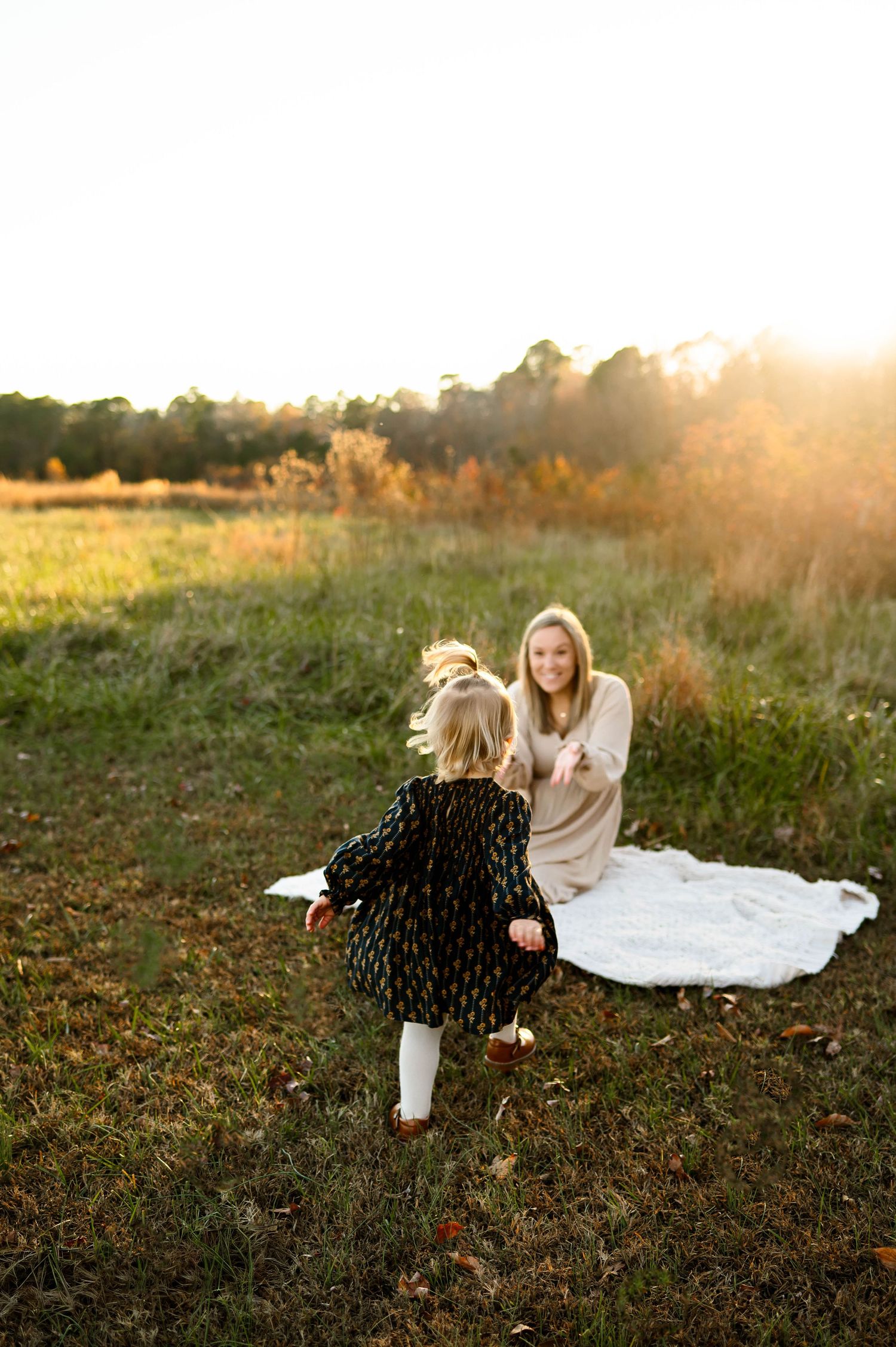 Mother reaching for toddler in a sunlit field during golden hour family photo session with Raleigh family photographer