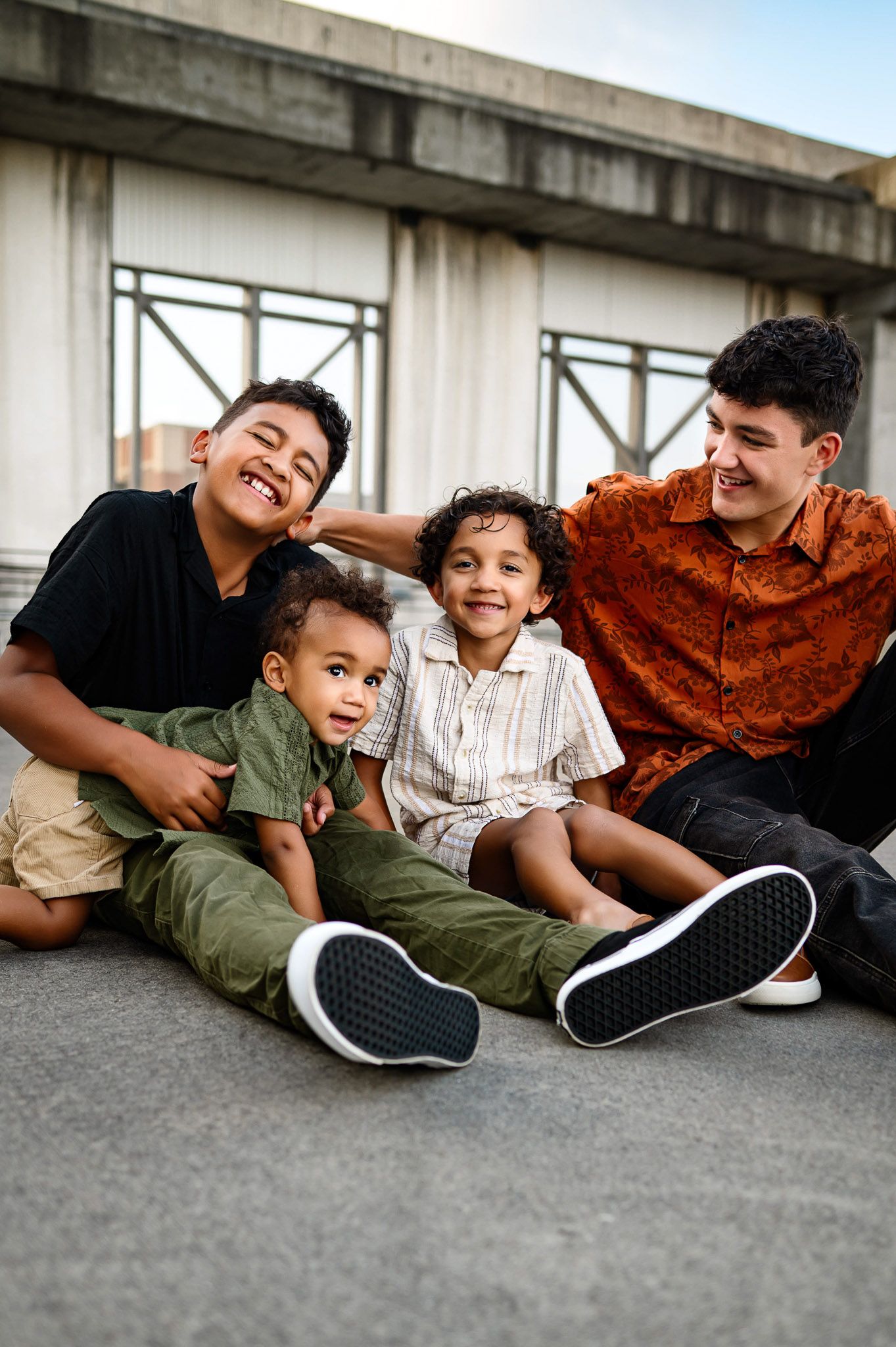 Four siblings sitting together and laughing during a playful urban family photography session in Durham NC