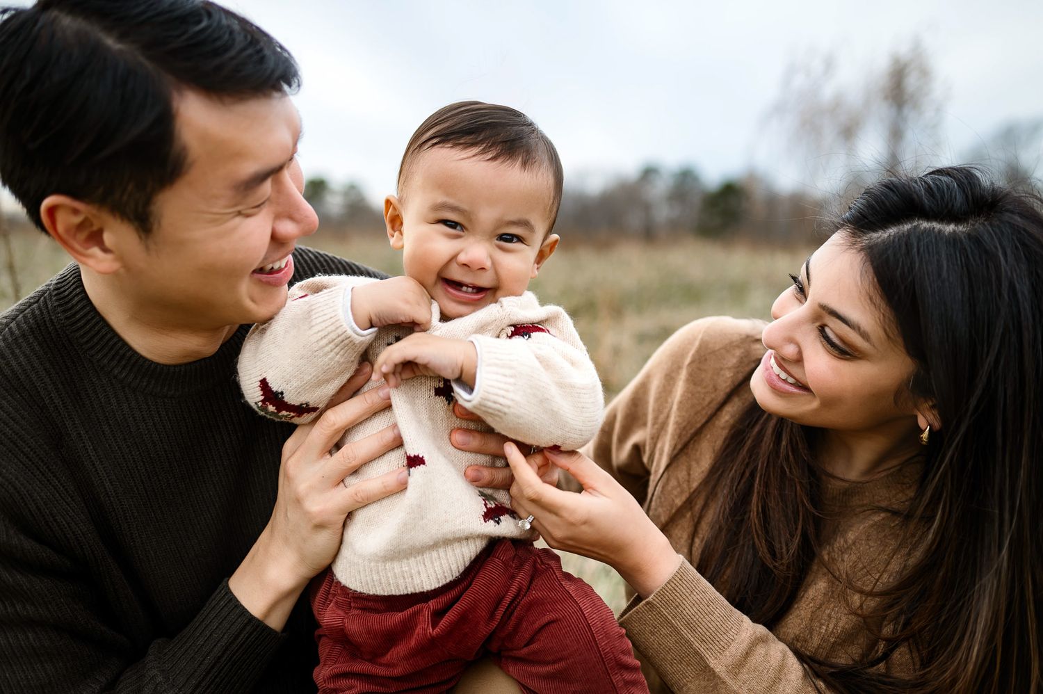 Smiling baby sitting between parents during a candid outdoor family photography session in Wake Forest NC