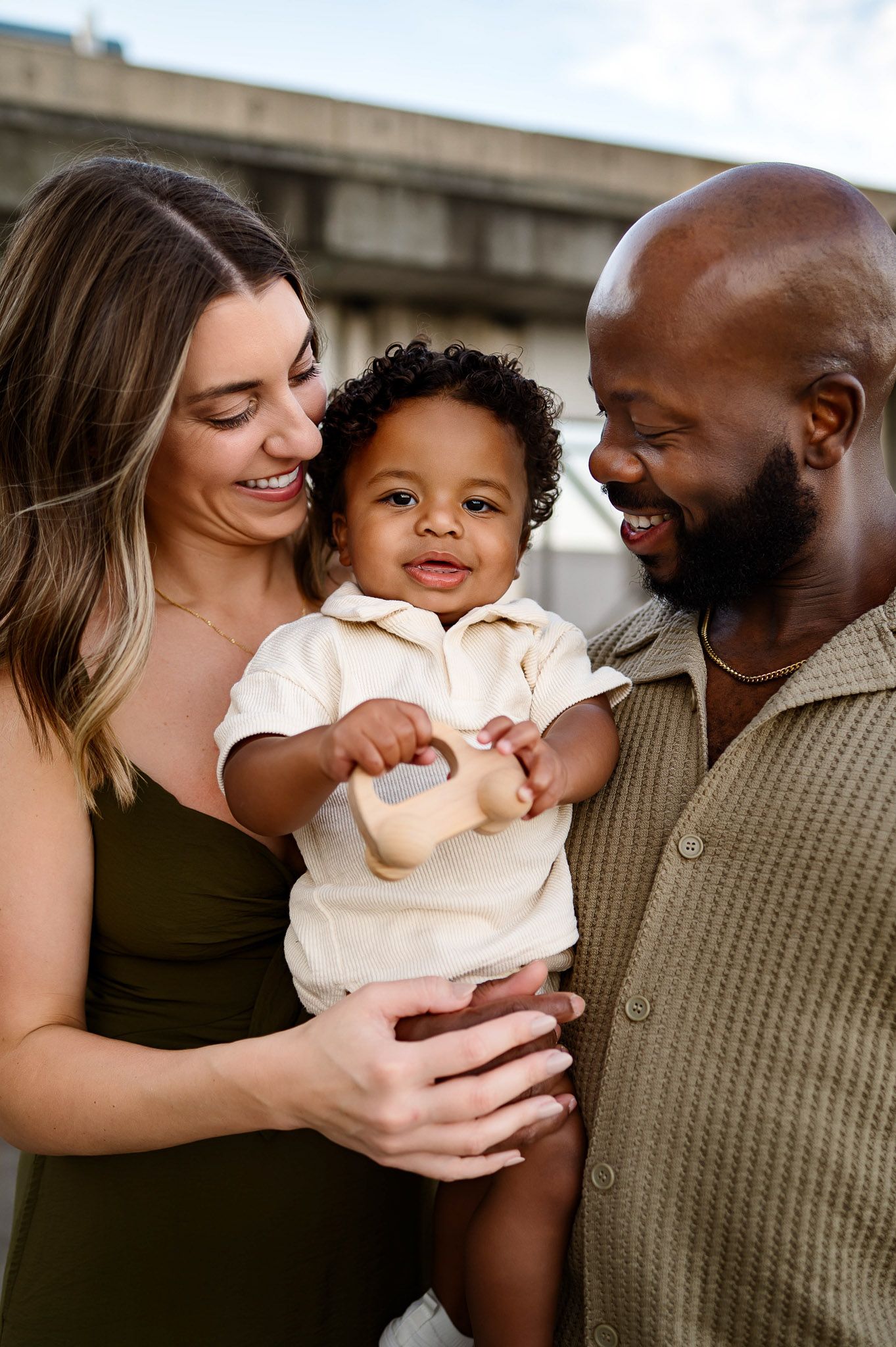 Parents smiling while holding their toddler during an urban family photography session in downtown Raleigh