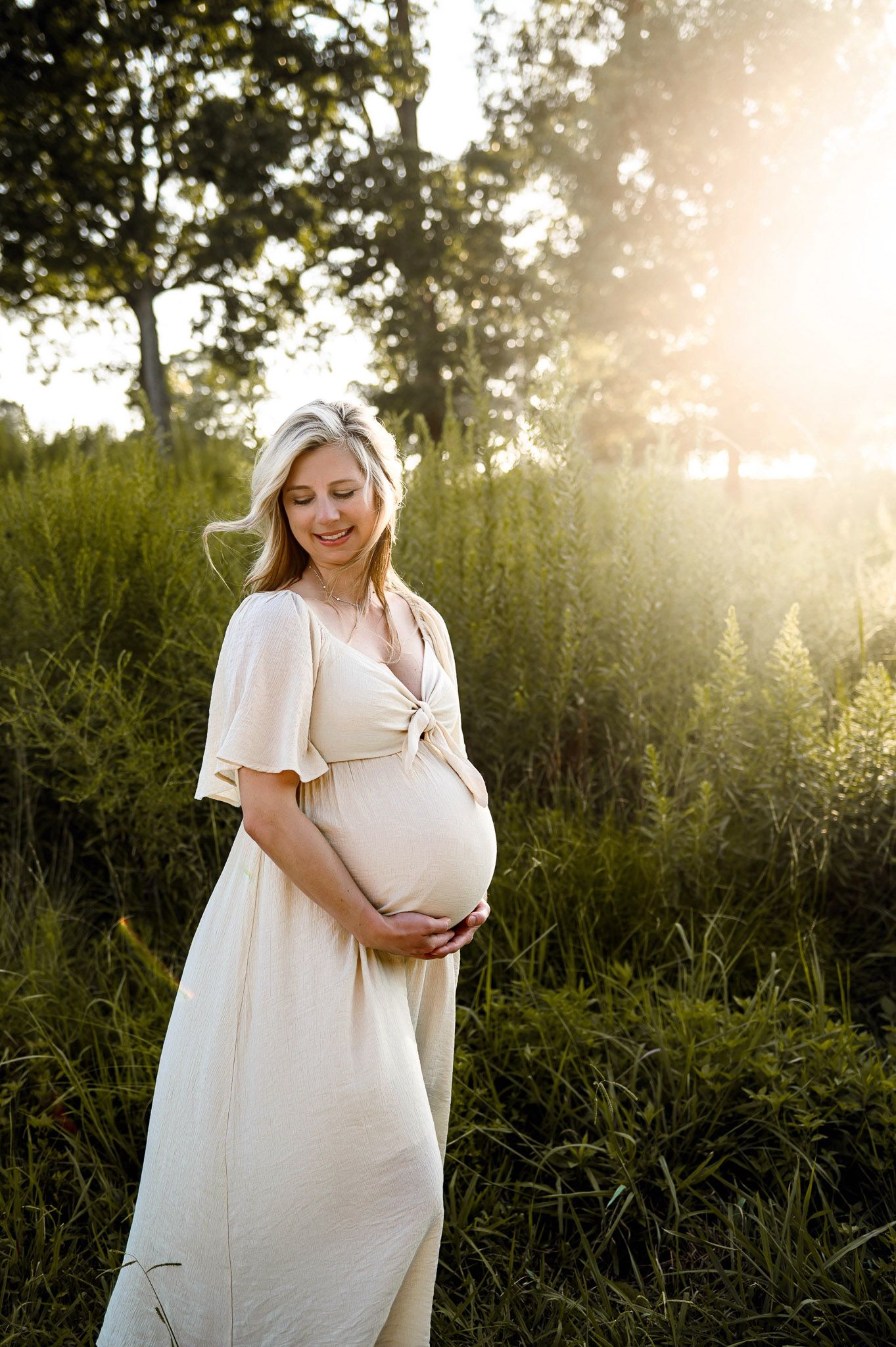 Raleigh maternity photographer capturing a pregnant mother standing in tall grass during golden hour