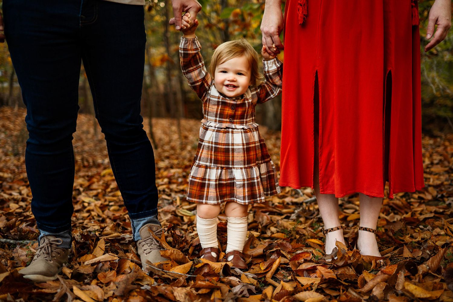 Smiling toddler holding both parents hands during a fall family photography session in Raleigh NC