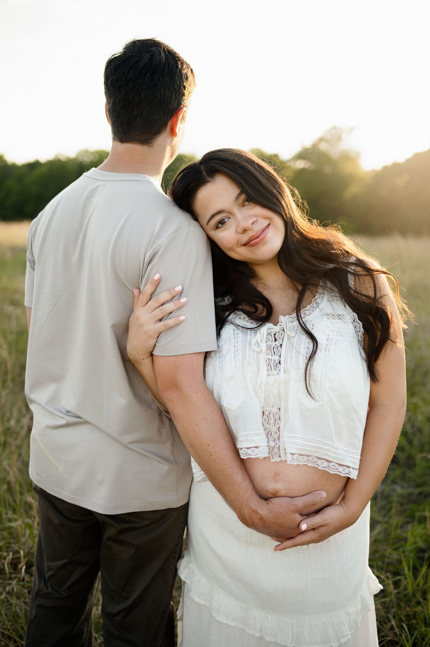 Mother cuddles with her husband's arm while showing her bare skinned pregnant belly during a maternity photoshoot in Raleigh NC