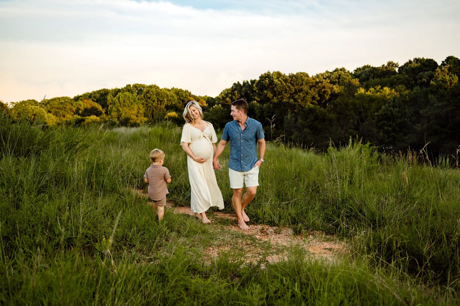 Expecting parents walking with toddler during relaxed outdoor photography session with Raleigh maternity photographer