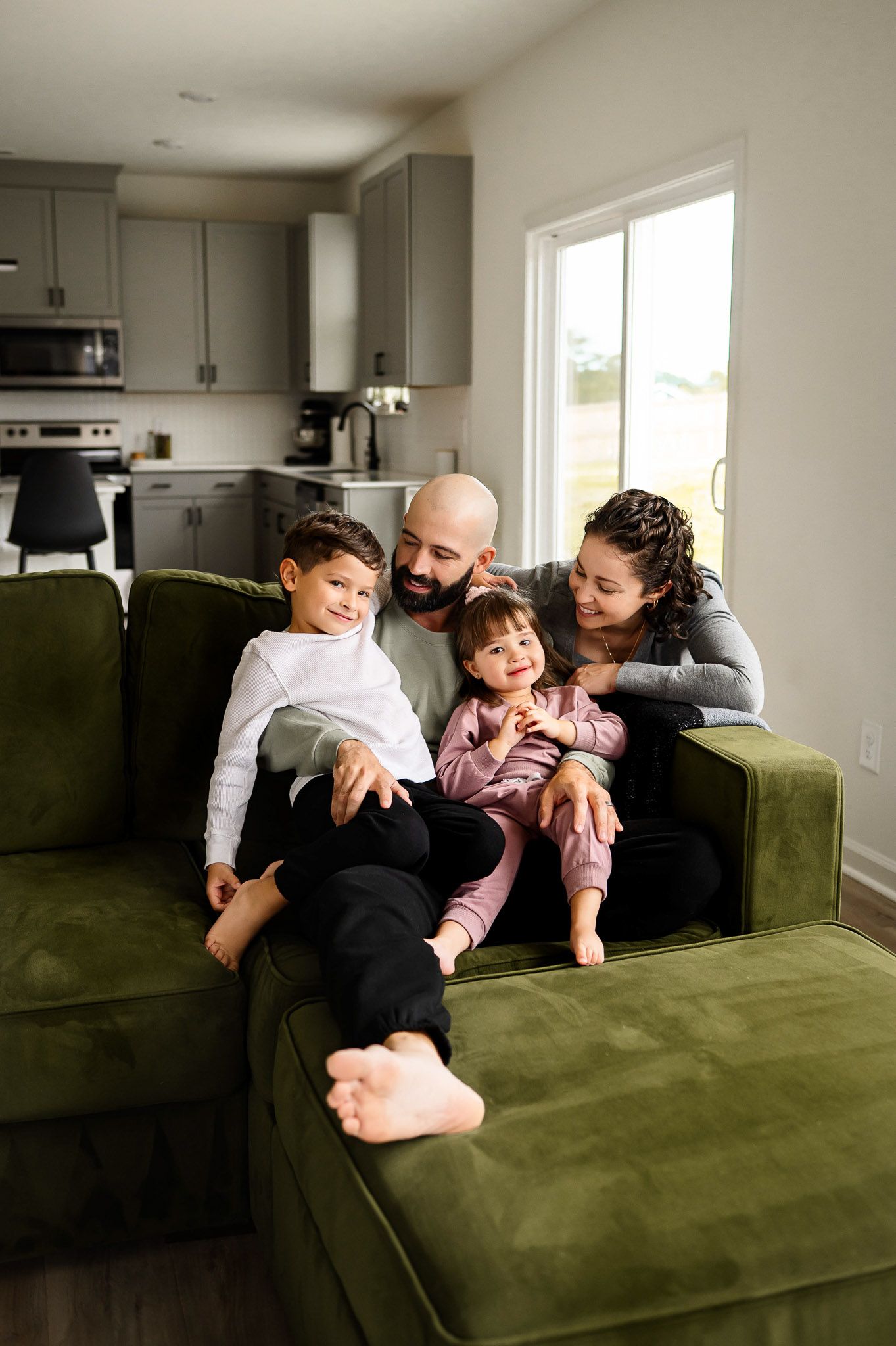 Parents and young children cuddling on couch during natural light in home family photography session in Raleigh NC