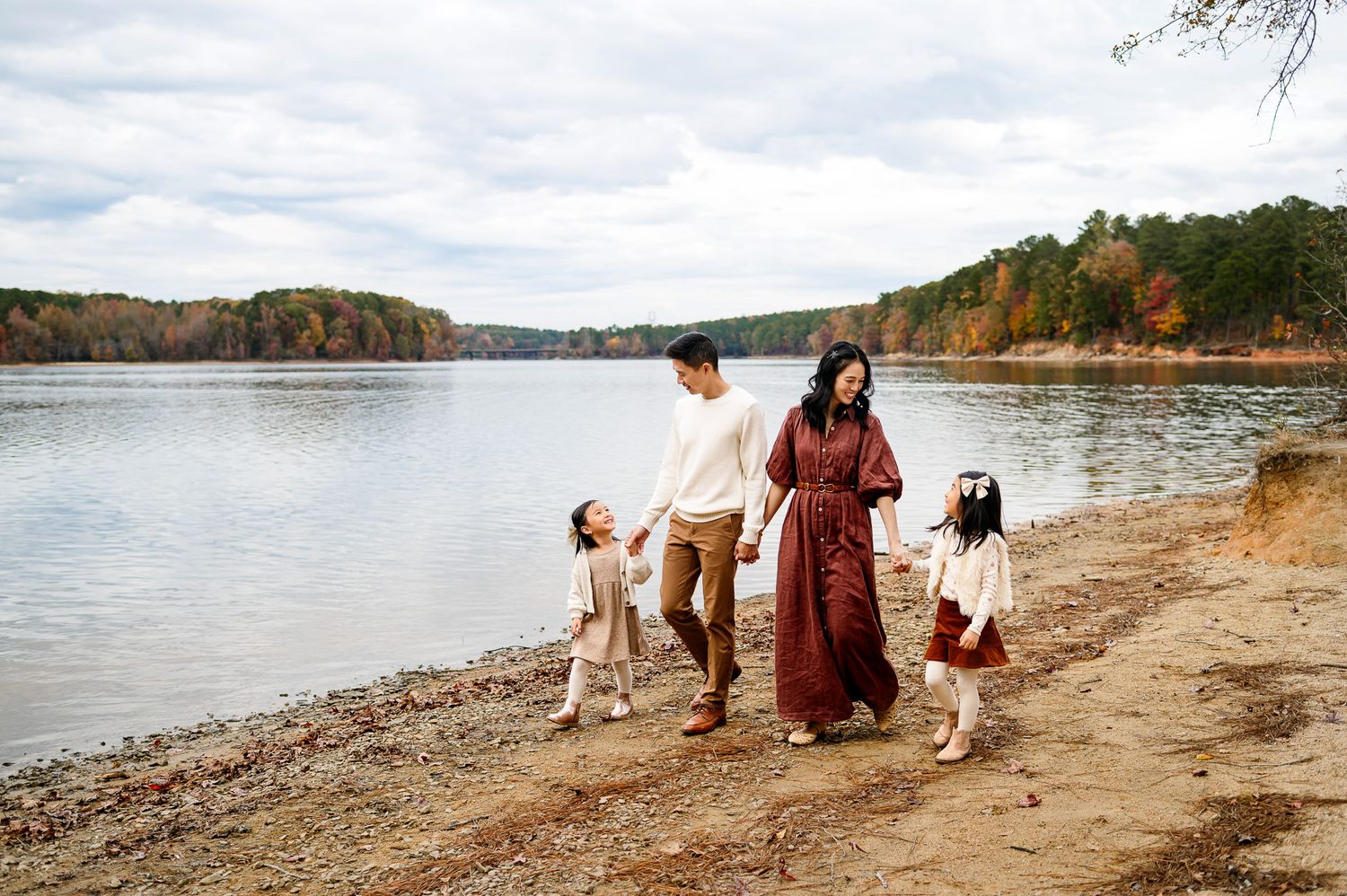Parents walking with their two daughters along the water during a lakeside family photography session in the Raleigh area