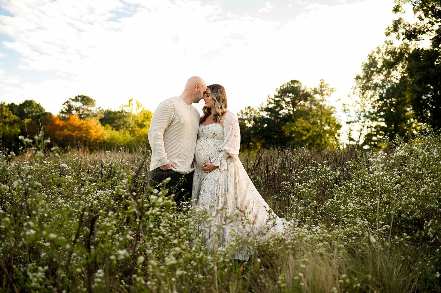 Raleigh maternity photographer capturing an expecting couple embracing in a wildflower field during golden hour