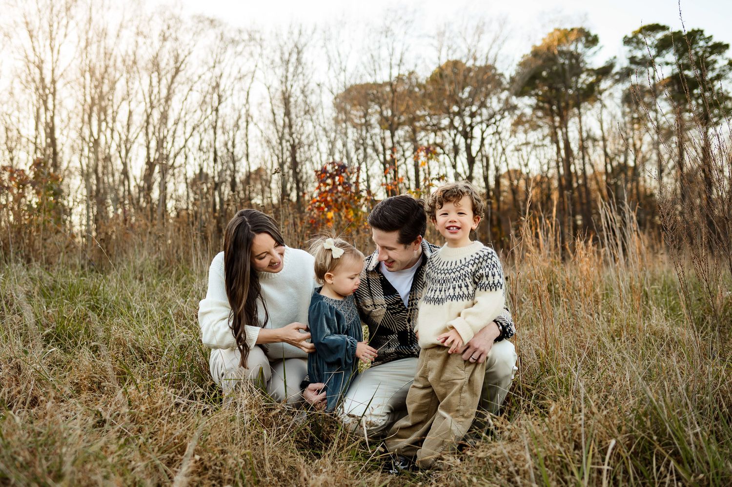 Family sitting together in tall grass during a relaxed outdoor family photography session in Cary NC