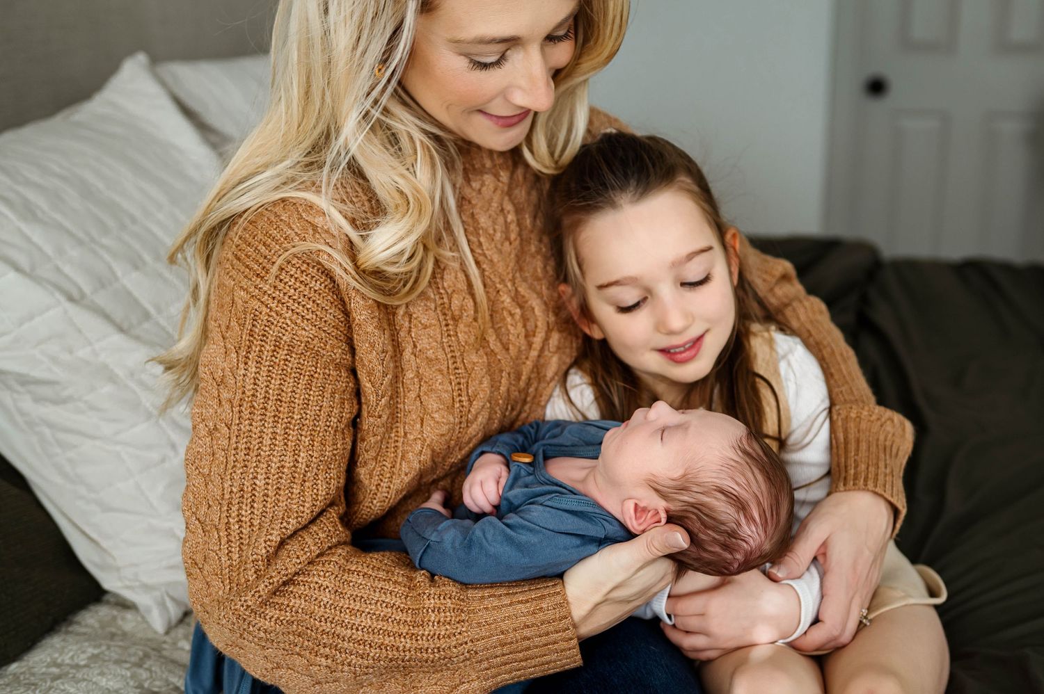 Mother and older sister holding a newborn during a relaxed in-home newborn photography session in Raleigh NC