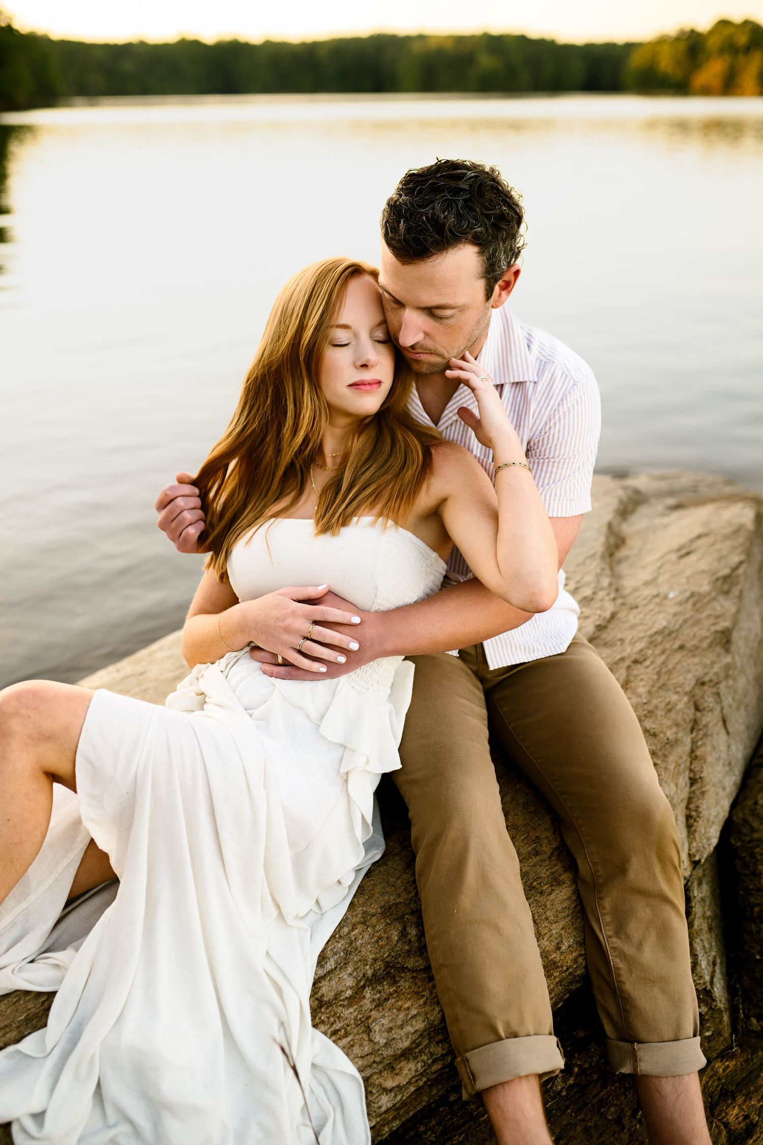 Romantic couple embraces on rocks by serene lake at sunset during family photography session with Emma Branch Photography