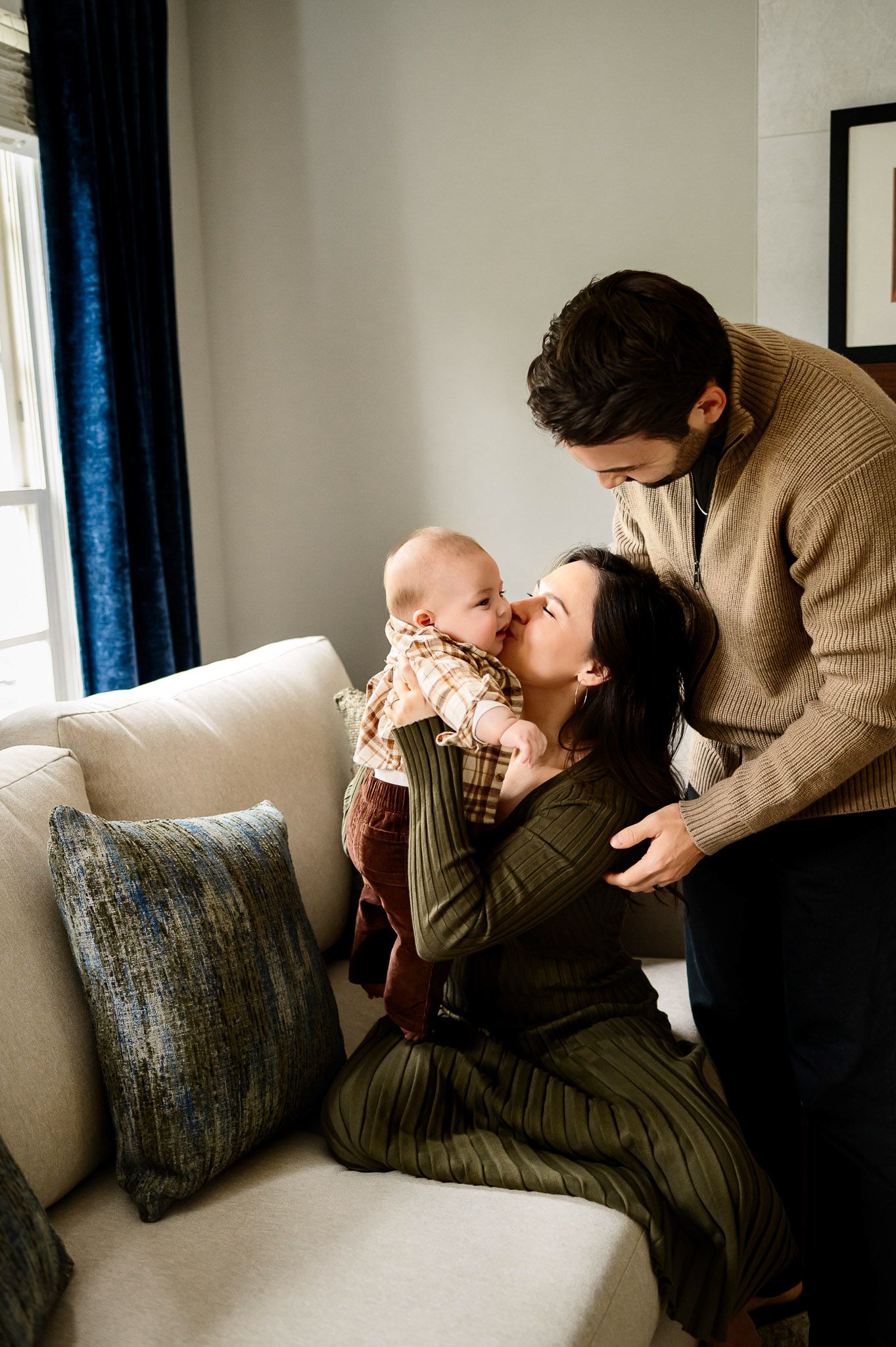 Mother kissing her baby while father looks on during a natural in-home family photography session in Raleigh, North Carolina
