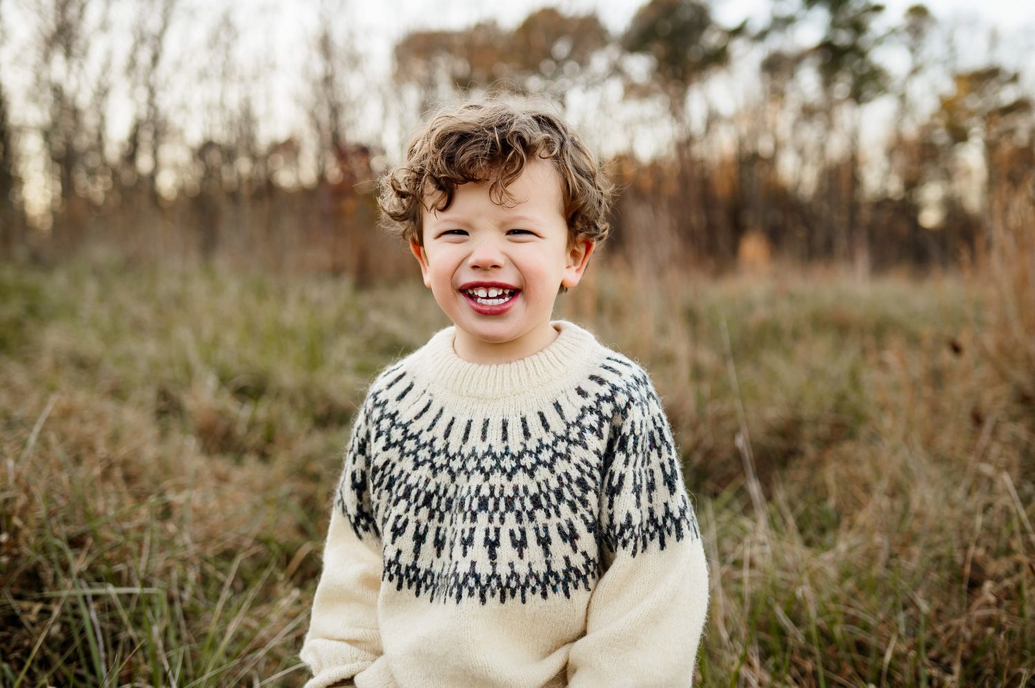 Smiling toddler boy standing in a grassy field during an outdoor lifestyle family photography session near Wake Forest
