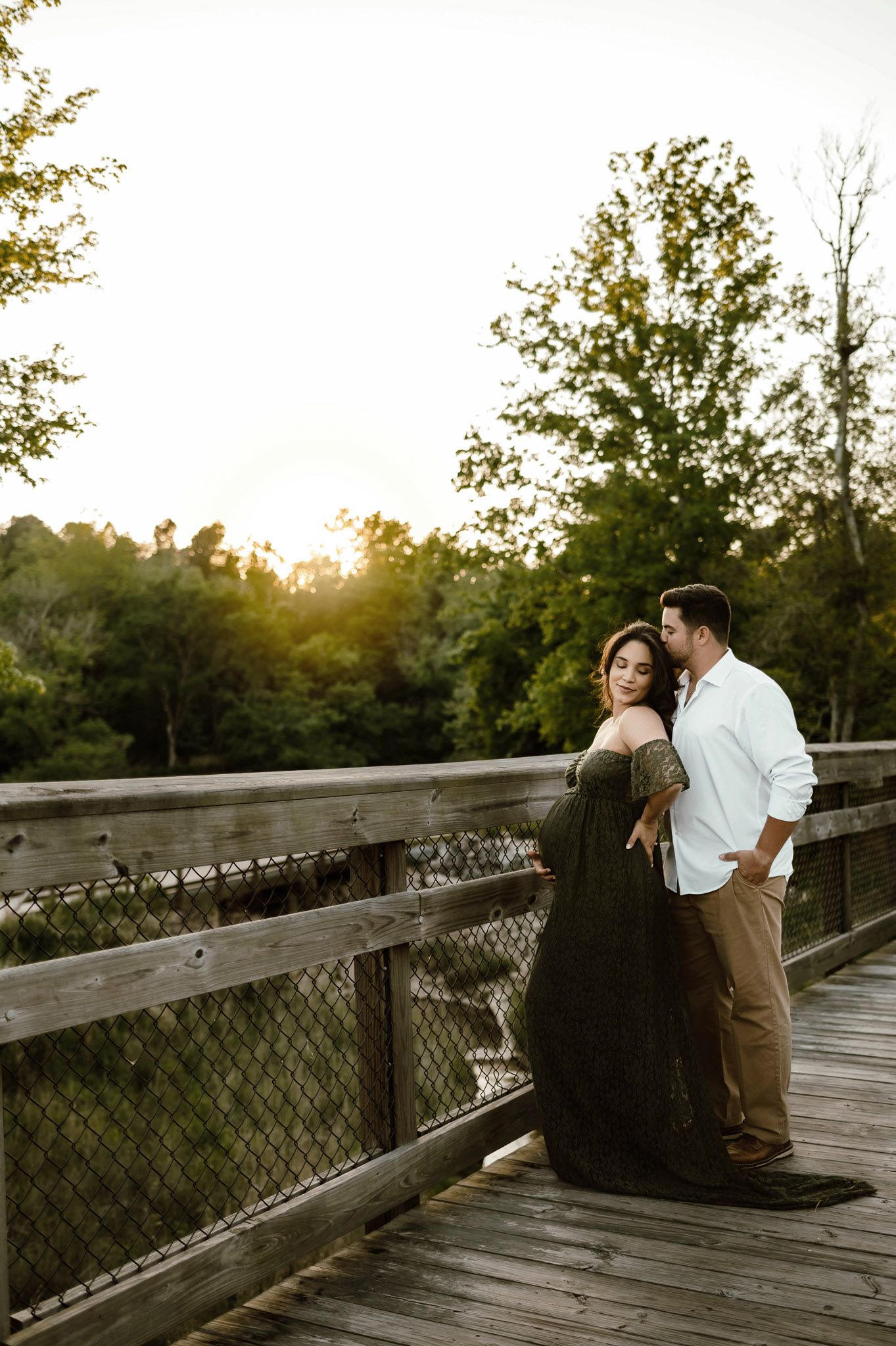 Expectant couple standing together on a wooden bridge during a maternity photography session near Durham NC