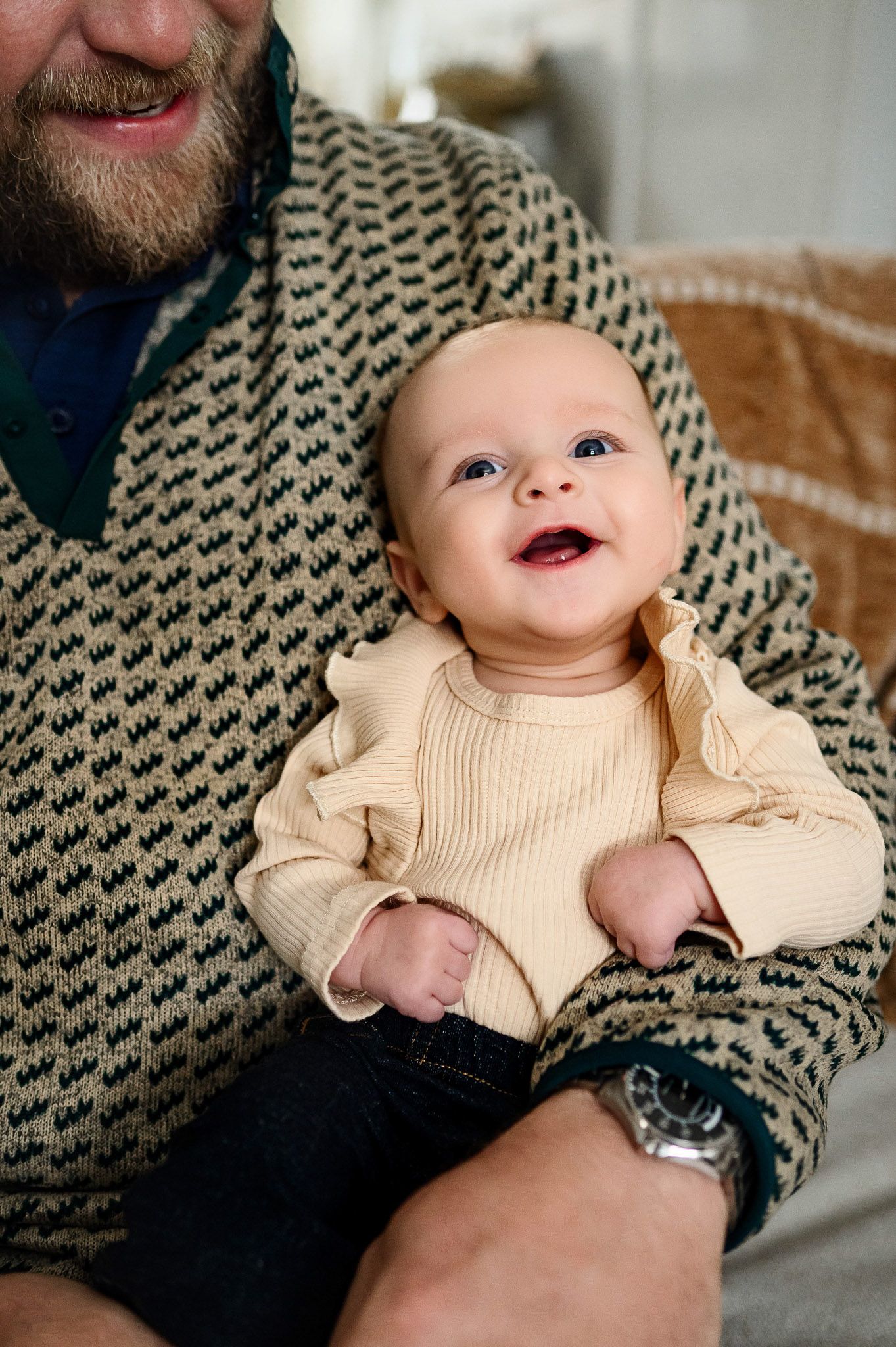 Close-up portrait of a smiling baby sitting on their father’s lap during an in-home family photography session