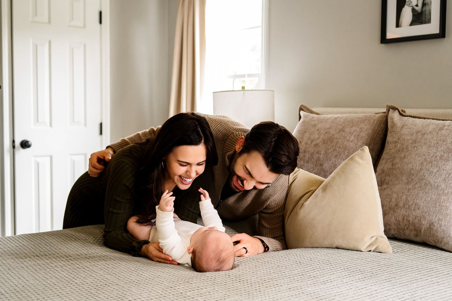 Parents playing with their baby together on a bed during a relaxed in-home lifestyle family photography session in Raleigh, North Carolina