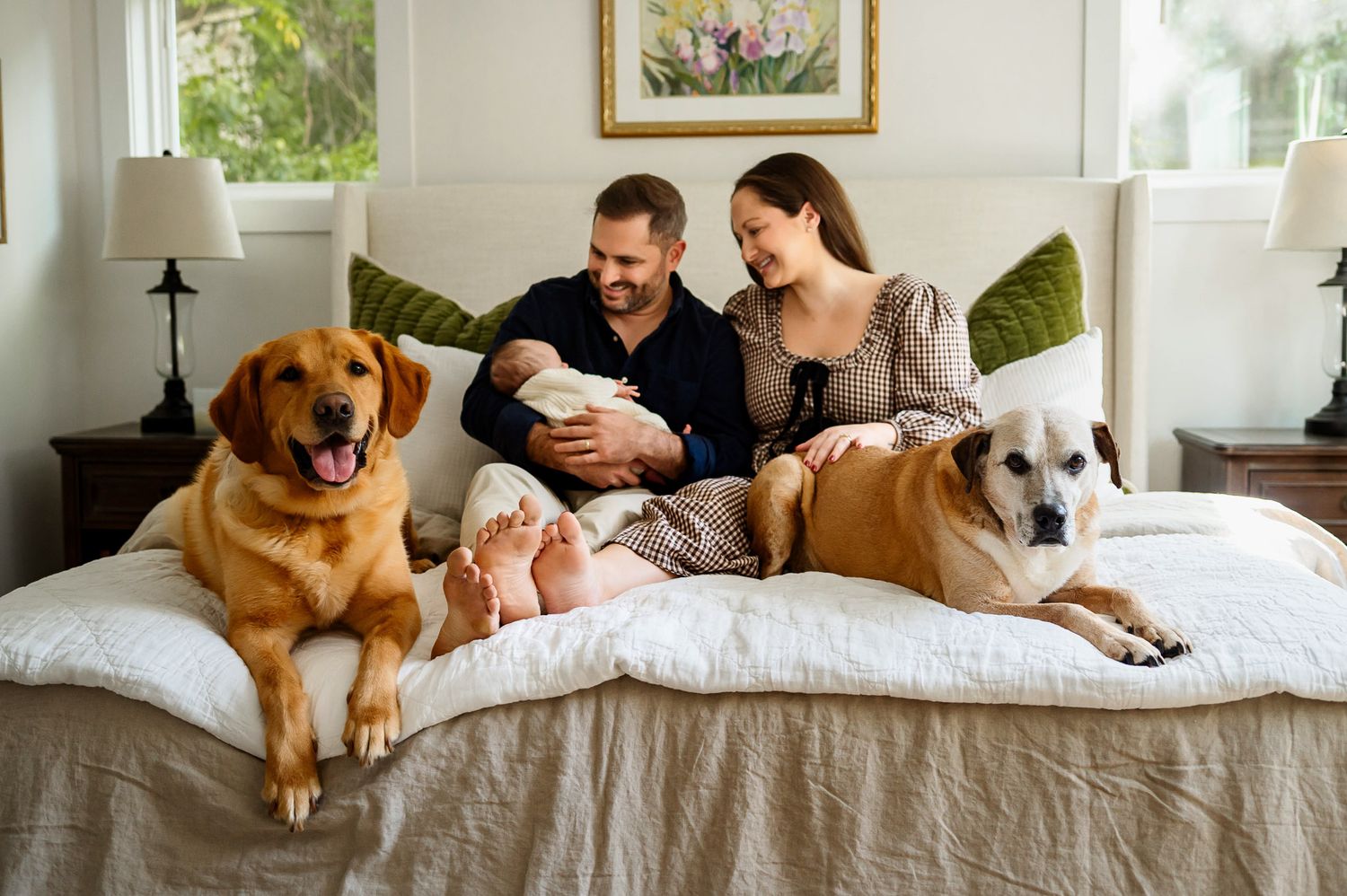 Parents holding newborn on bed with family dogs during cozy newborn photography session in Wake Forest NC