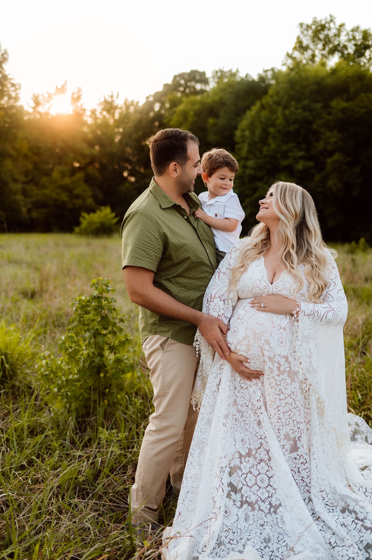 Beautiful maternity photo in field during golden hour sunset of family in white lace gown with best raleigh maternity photographer