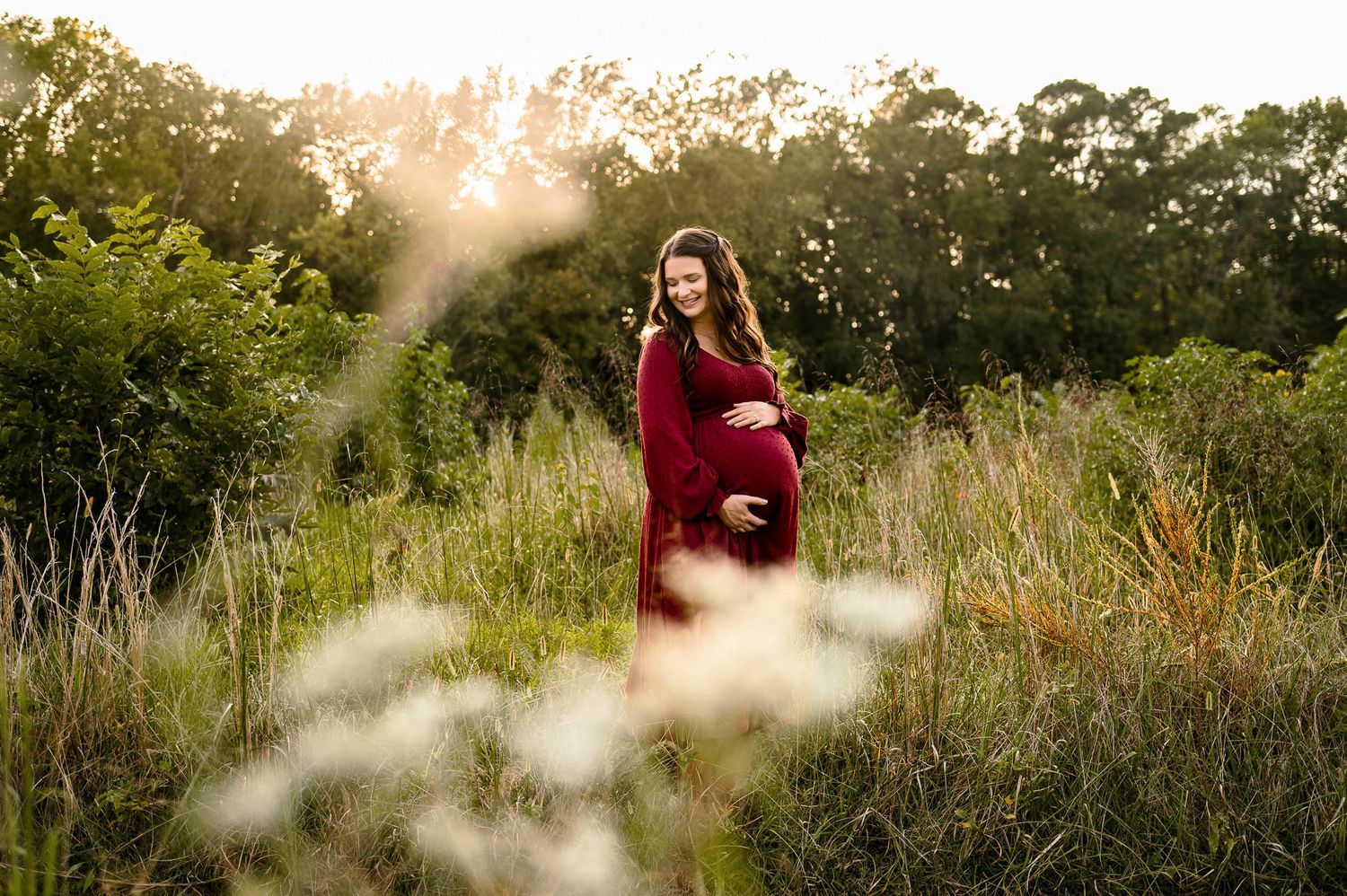 Expectant mother in a red dress during golden hour maternity photography session in a grassy field in Raleigh NC
