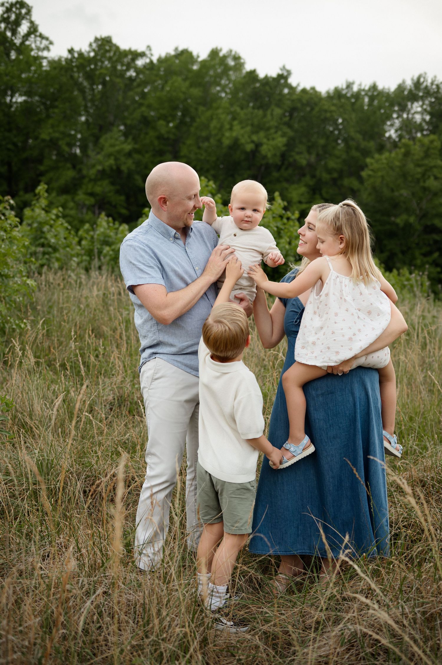 Family of five standing together in a grassy field during a Raleigh family photography session with parents holding their youngest children