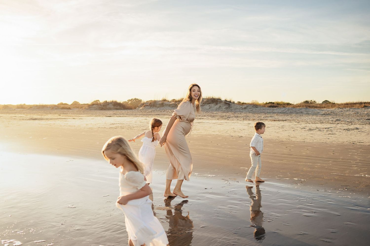 Mother and young children run playfully around each other on beach laughing at sunset with Raleigh maternity photographer Emma Branch