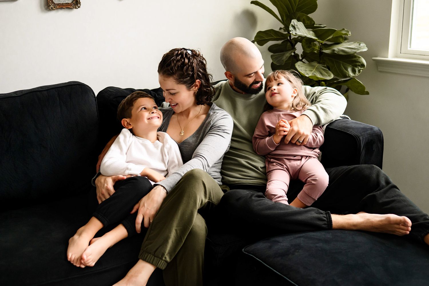 Parents relaxing with young children on couch during natural in-home family photography session in Cary NC