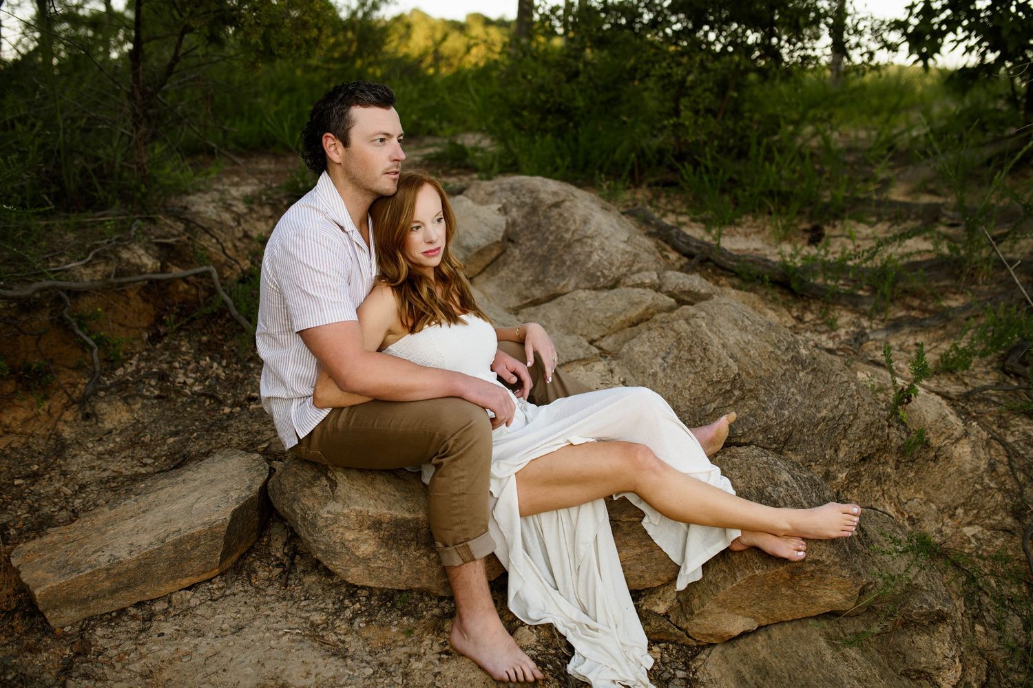 Couple sitting on rocky outcrop in forest during romantic outdoor family photo session in Wake Forest NC with family photographer