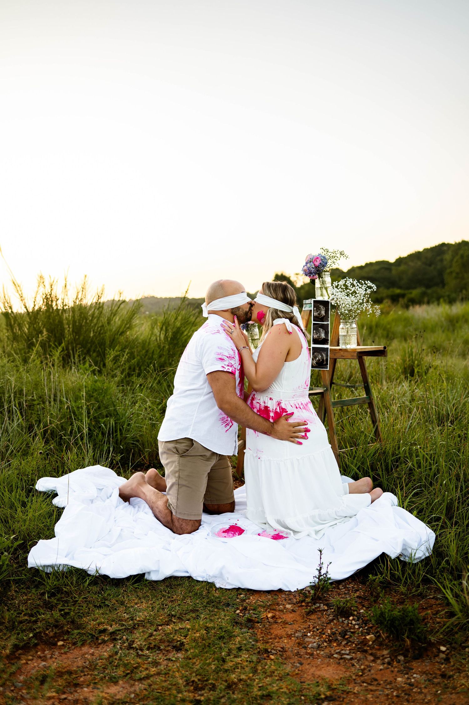 Expecting parents kneeling together and kissing  during a gender reveal photography session with a Raleigh family photographer