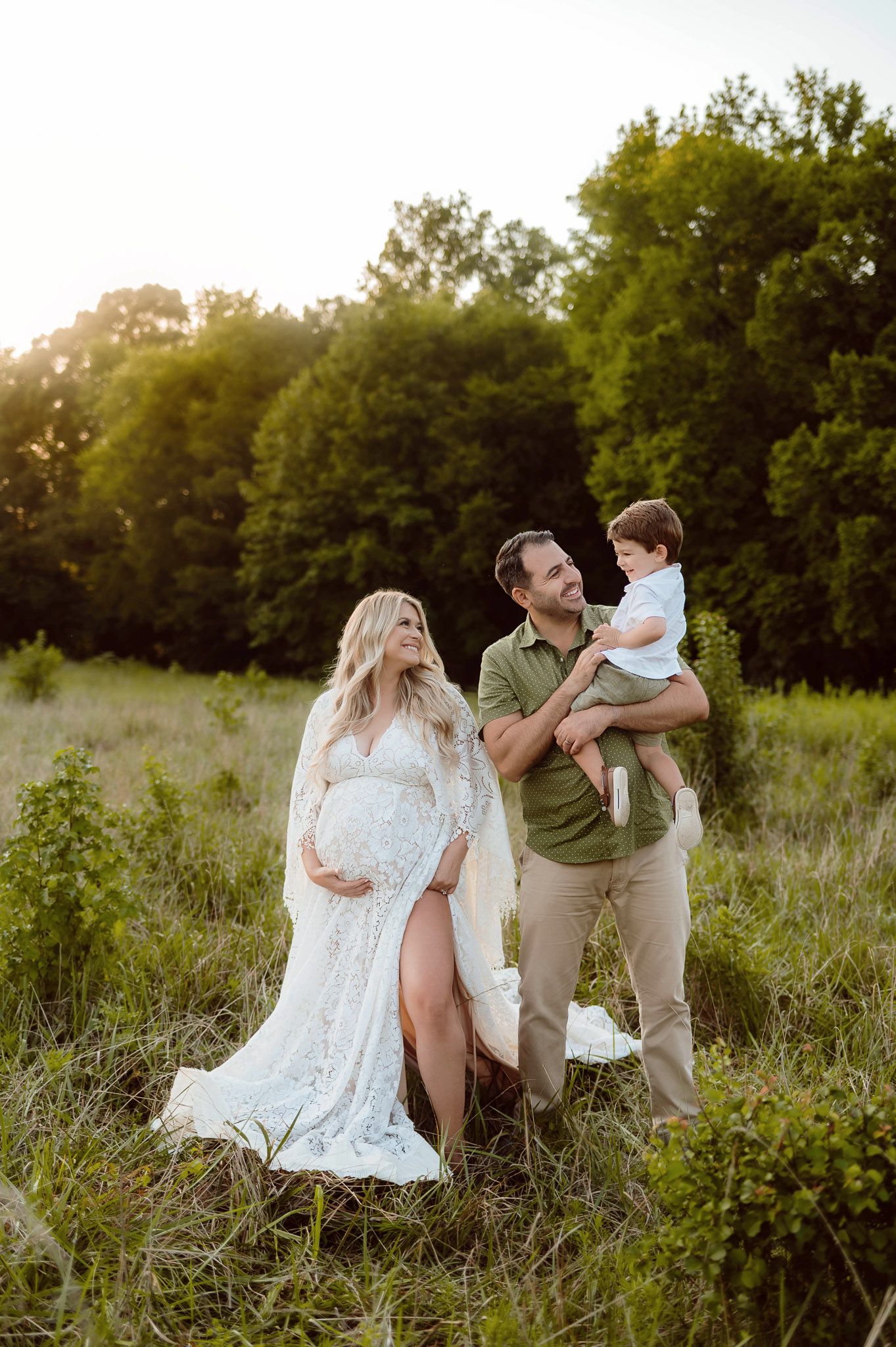 Expectant mother in a lace maternity gown standing with her partner and young son during a sunset maternity photography session in Raleigh